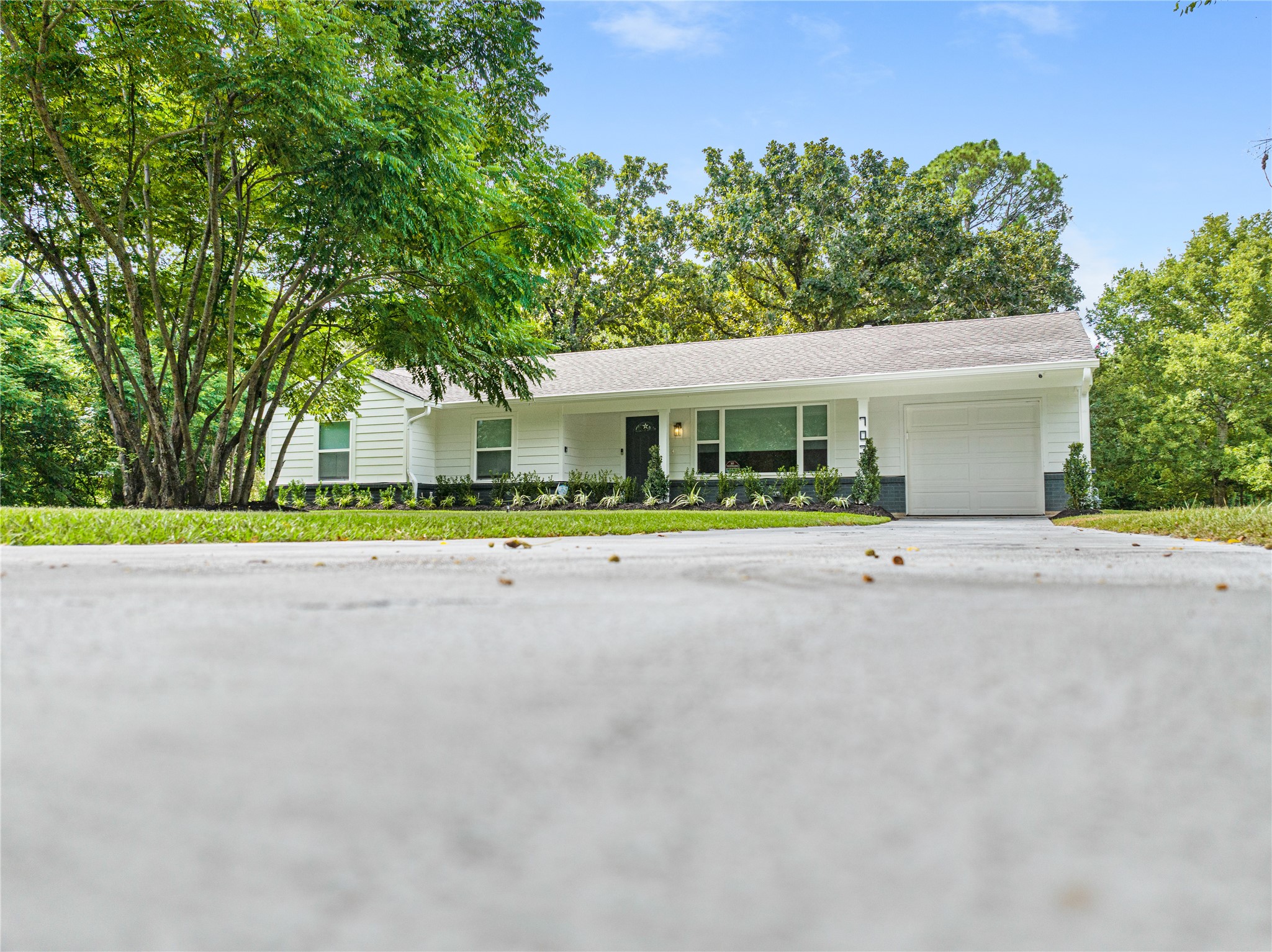 Wide front exterior view showcasing the home's single-story design, mature trees, and generous driveway area.