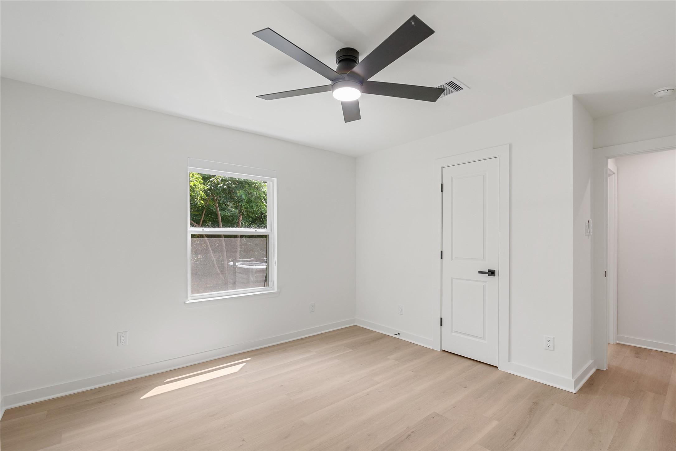 Another angle of the bedroom highlighting the natural light, modern ceiling fan, and access to the adjoining hallway.