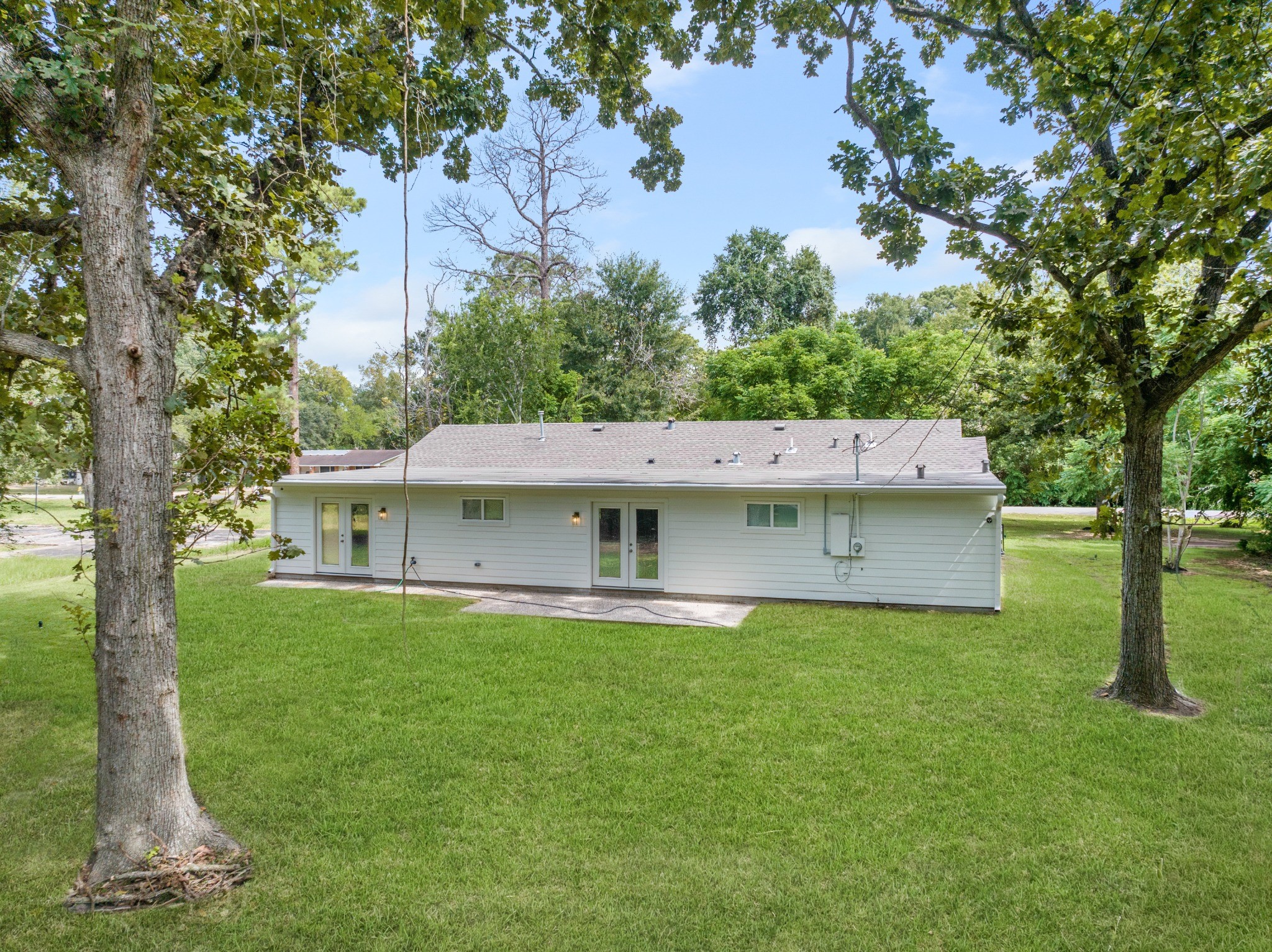 Side view of the home framed by mature shade trees and expansive lawn, highlighting the property's spacious setting.
