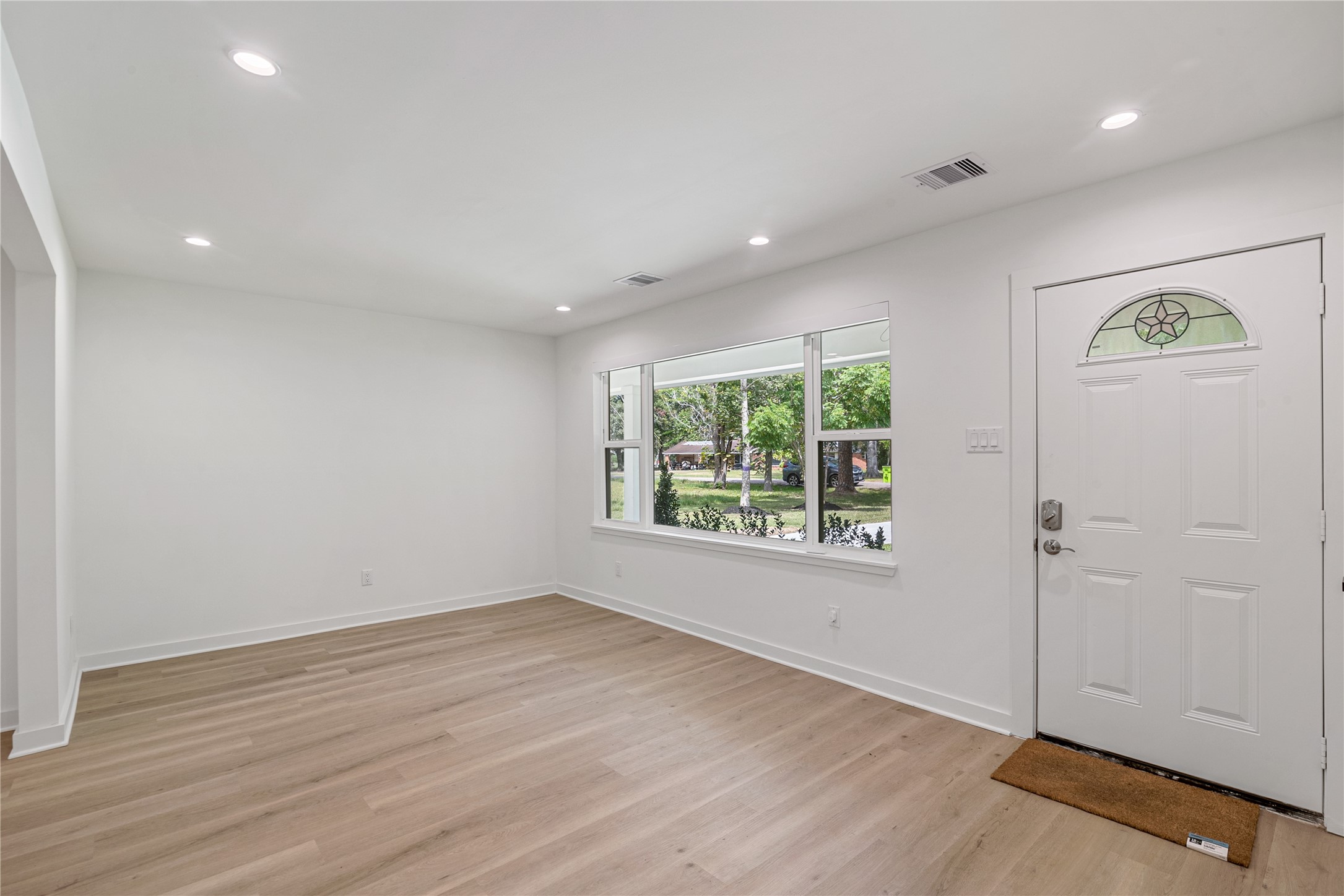 Welcoming front living area with updated flooring, recessed lighting, and a large window overlooking the front lawn.