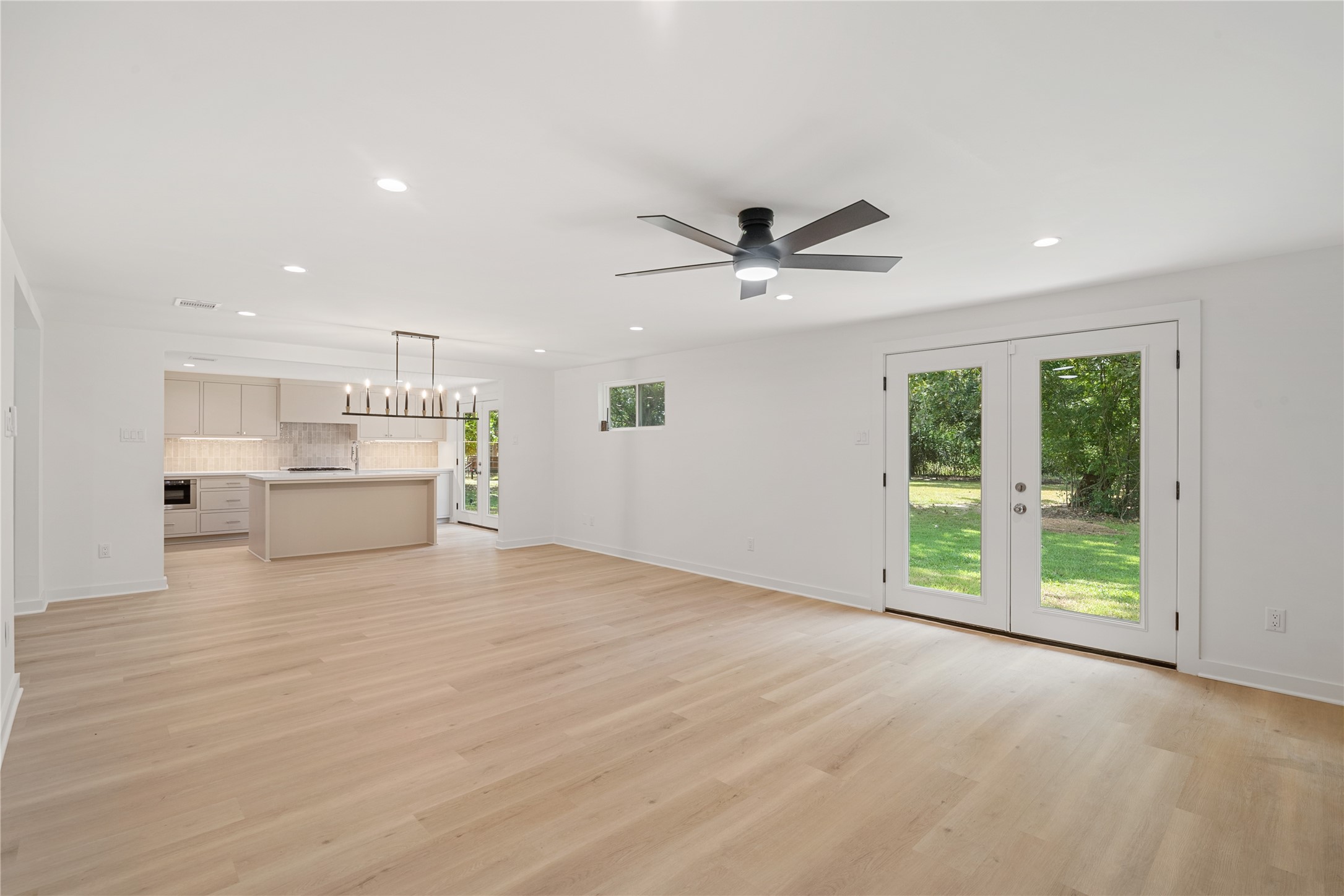 Open living room offers plenty of room to gather, with a modern ceiling fan and glass doors opening to the outdoor space.