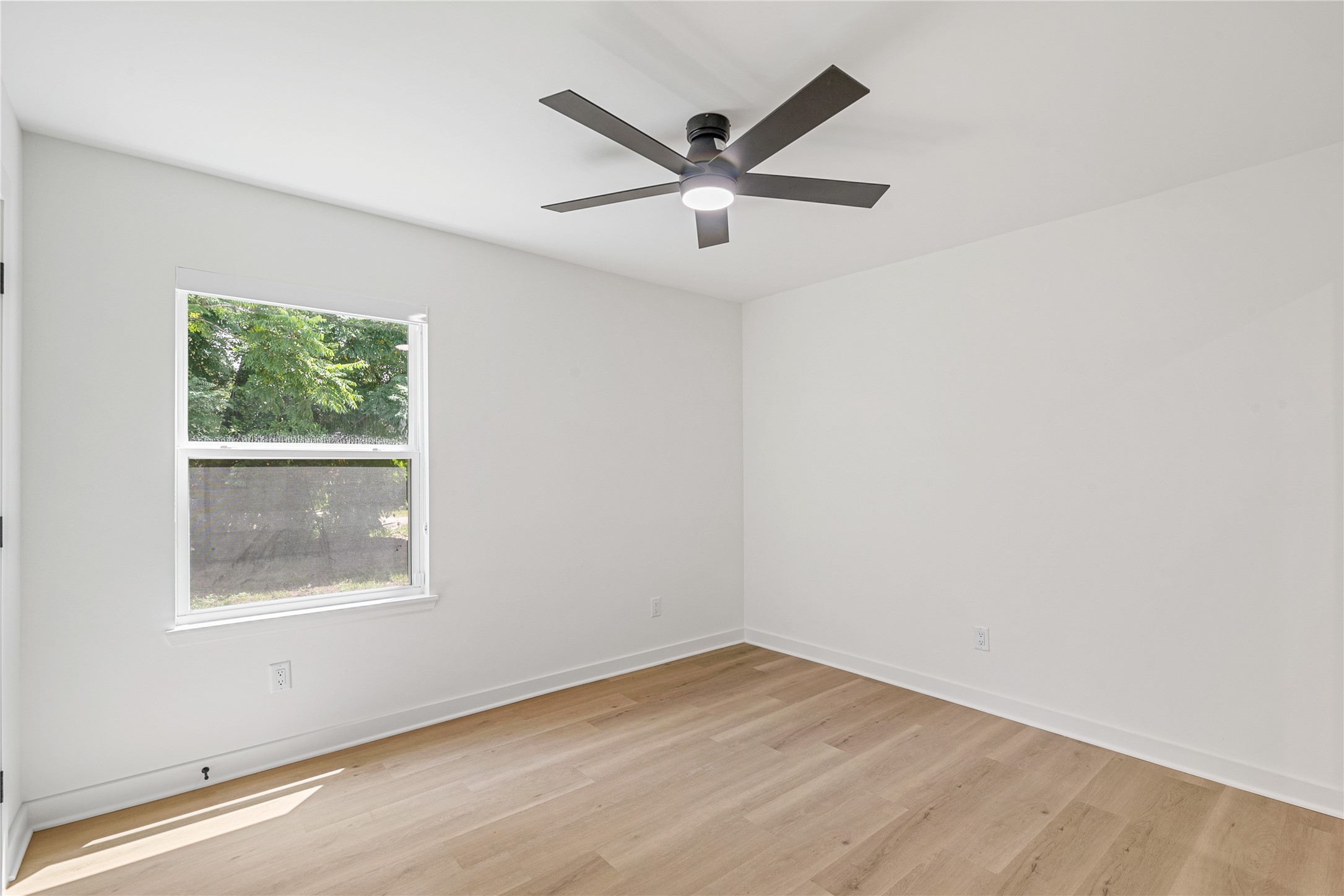 Additional bedroom view showcasing the updated flooring, neutral finishes, and window overlooking the greenery outside.
