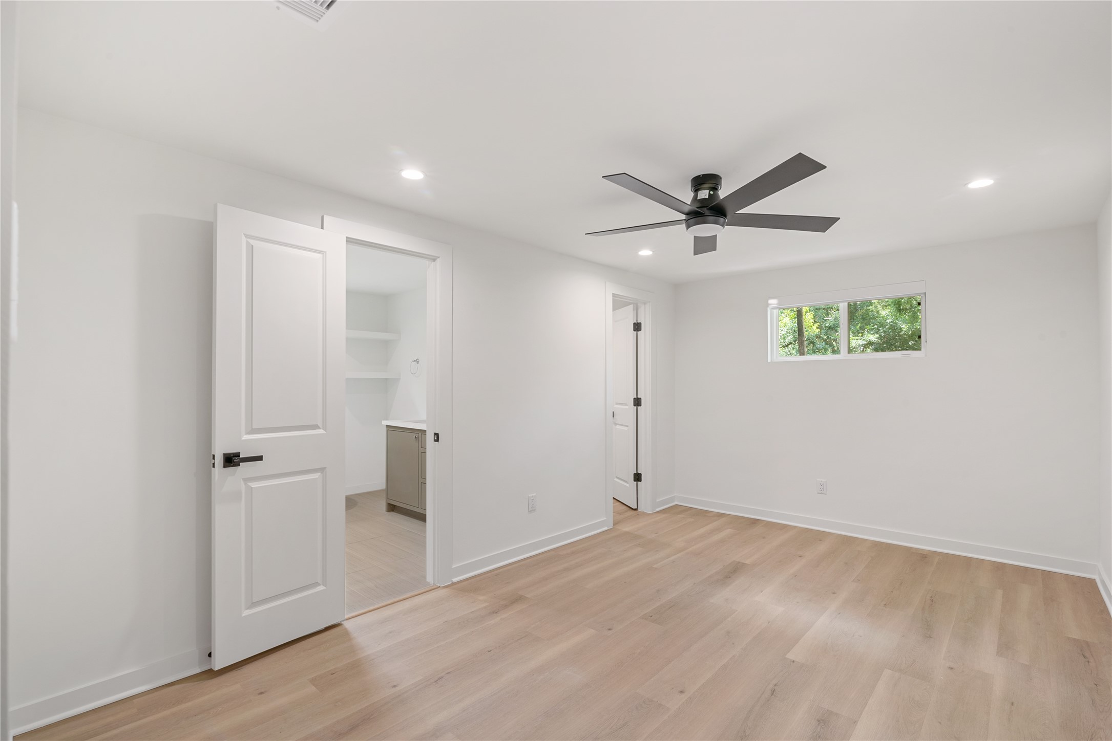 Spacious bedroom featuring updated flooring, a contemporary ceiling fan, and a window overlooking the greenery outside.