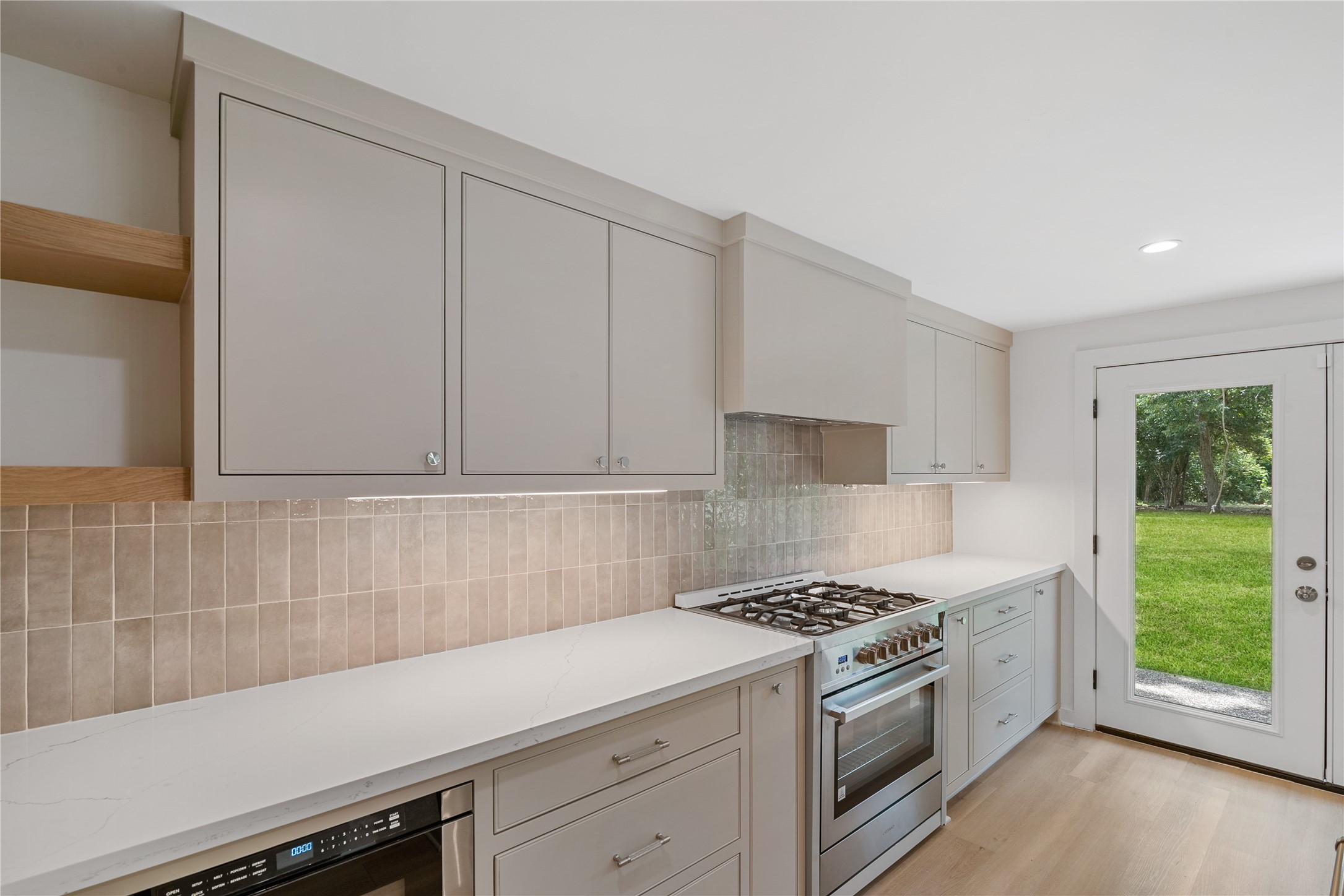 Additional kitchen view showcasing the quartz countertops, custom cabinetry, tile backsplash, stainless steel range, and access to the outdoors.