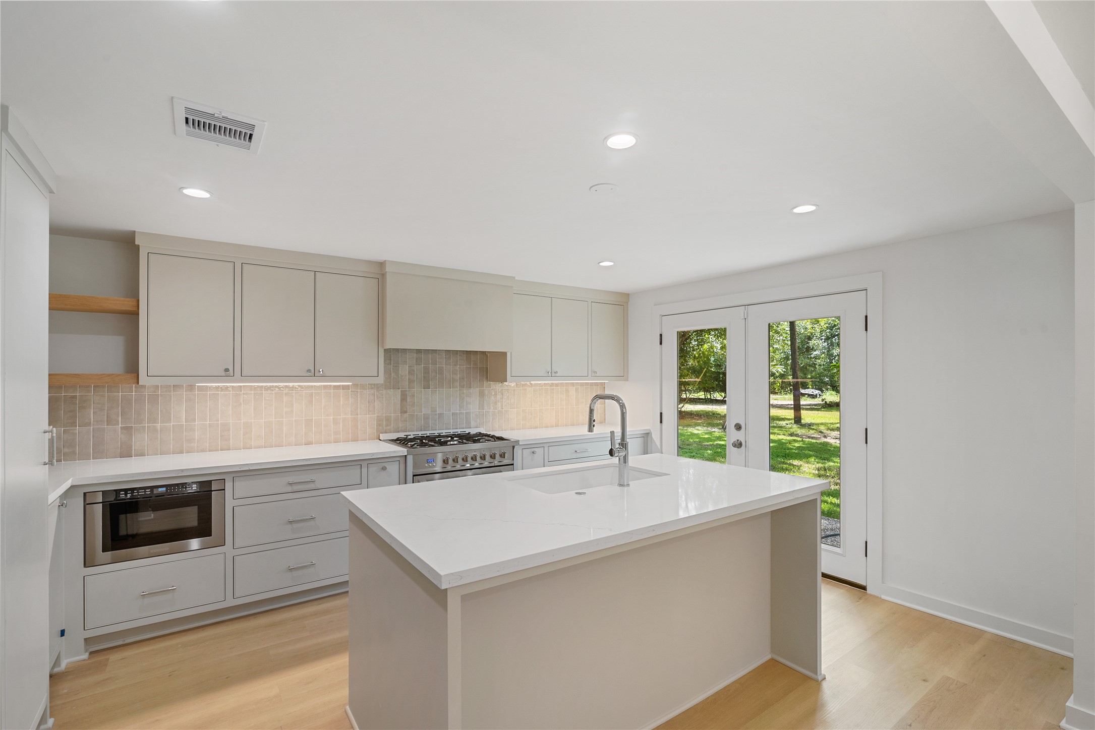 Additional kitchen view highlighting the quartz countertops, sleek finishes, and natural light from the adjoining exterior doors. Additional kitchen view highlighting the quartz countertops, sleek finishes, and natural light from the adjoining exterior doors.