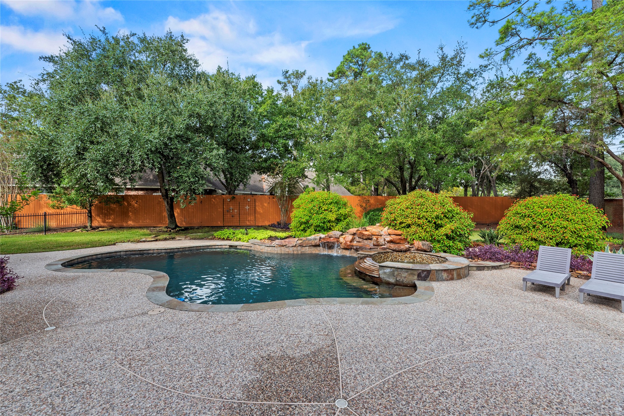 Freeform pool with cascading rock waterfall, raised spa, spacious decking and lush landscaping surrounded by mature trees.