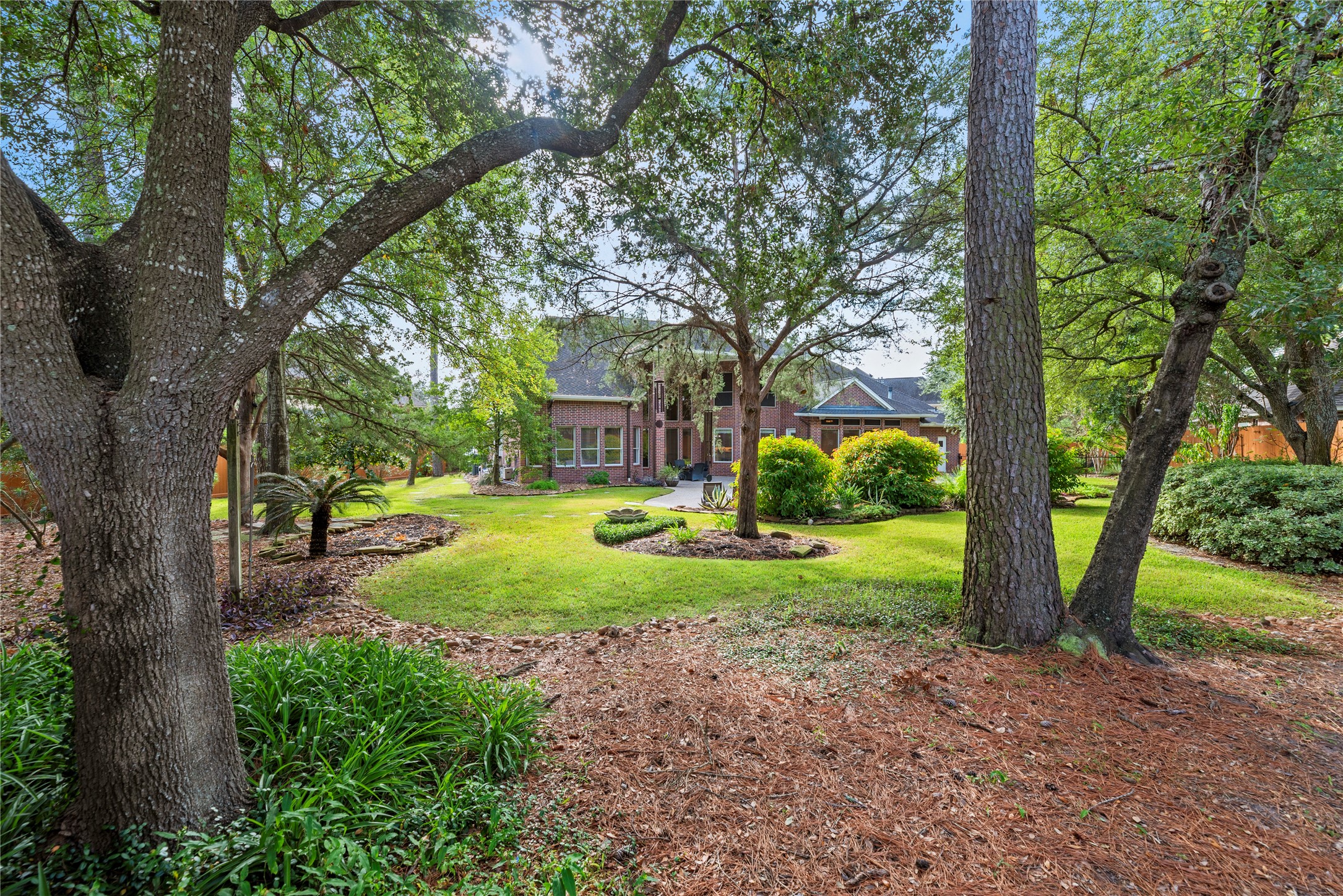 A picturesque view from the rear of the backyard showcases a park-like setting with towering mature trees, lush lawn and beautifully manicured landscaping, creating a serene and private retreat.
