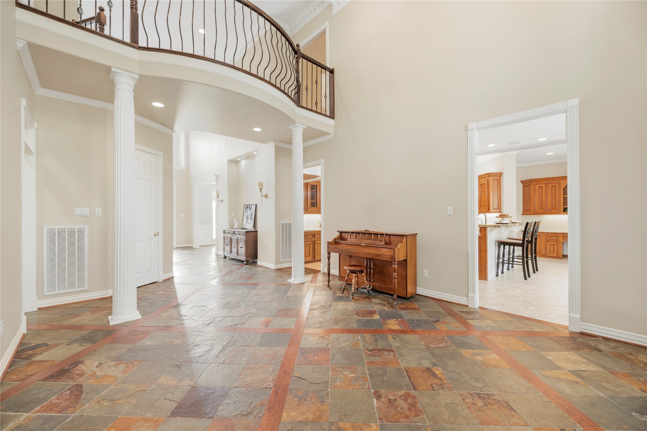 Impressive formal living room showcases a graceful curved balcony with decorative wrought iron railing, stately columns, elegant architectural detailing and rich slate flooring.