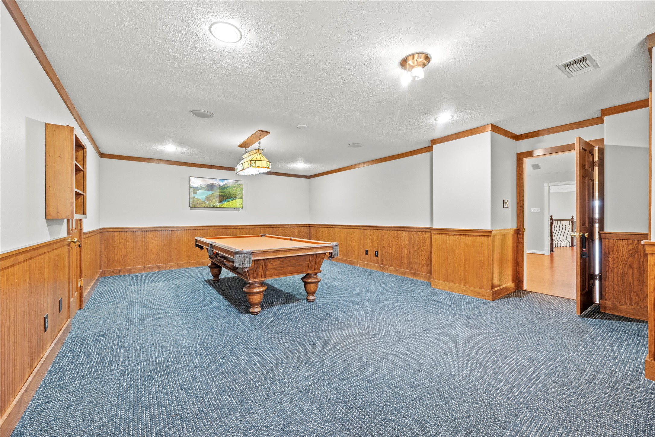 Upstairs bonus room featuring rich wood wainscoting, carpeted flooring and ample room for billiards, gaming and additional recreational activities.