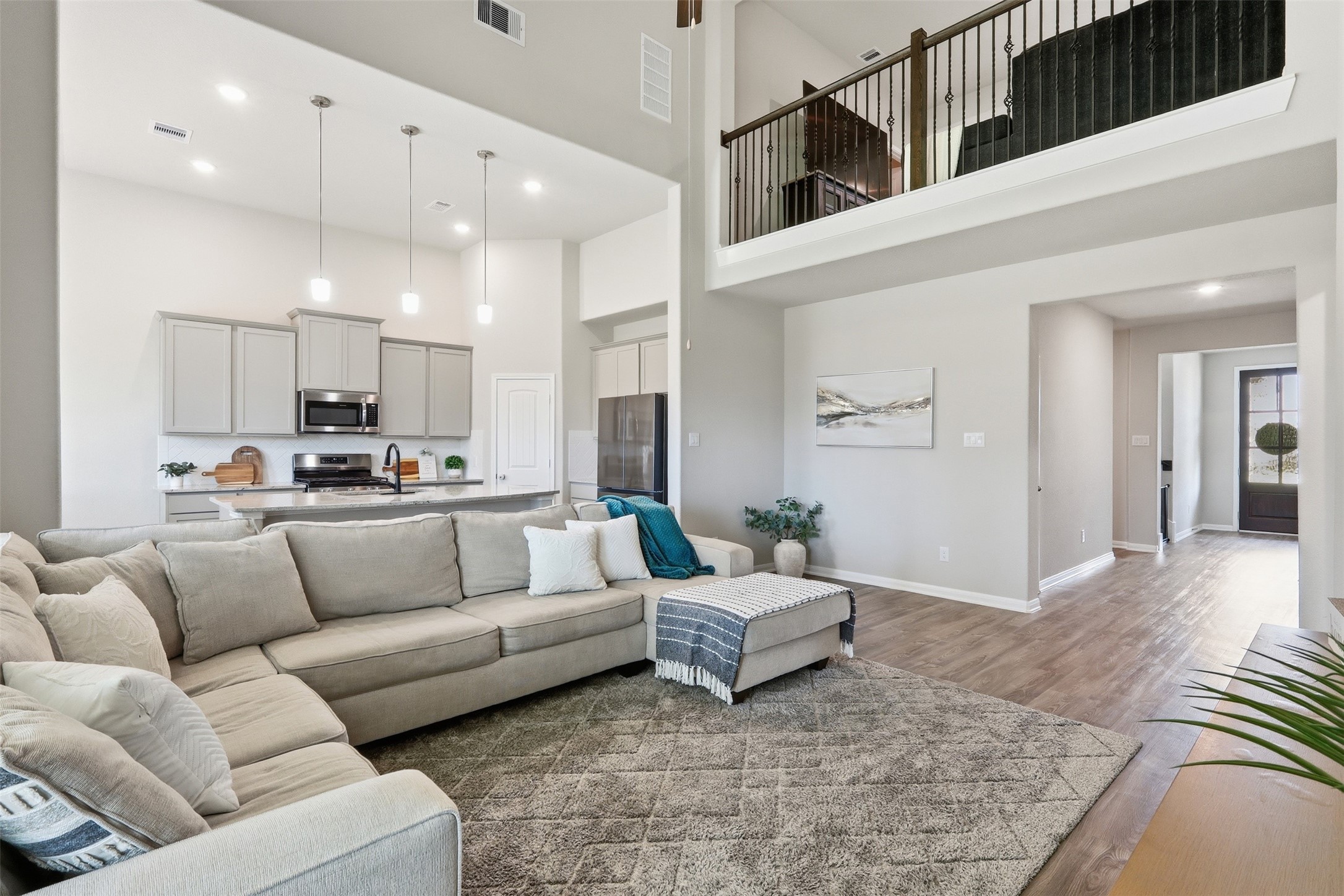 Open-concept living and kitchen area featuring soaring ceilings, stainless steel appliances, pendant lighting, abundant natural light, and views of the upstairs game room.