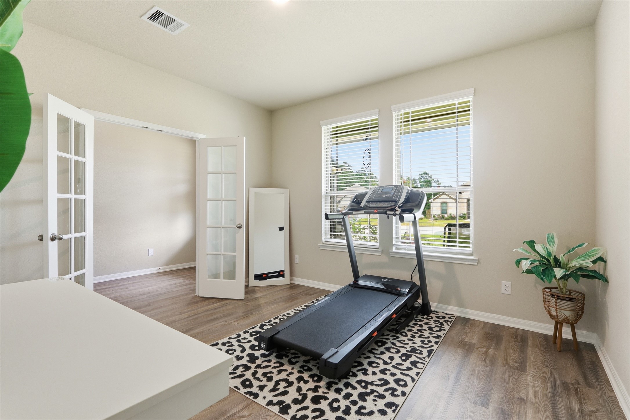 Flexible home office or study featuring elegant French doors, wood flooring, and large windows that fill the space with natural light.