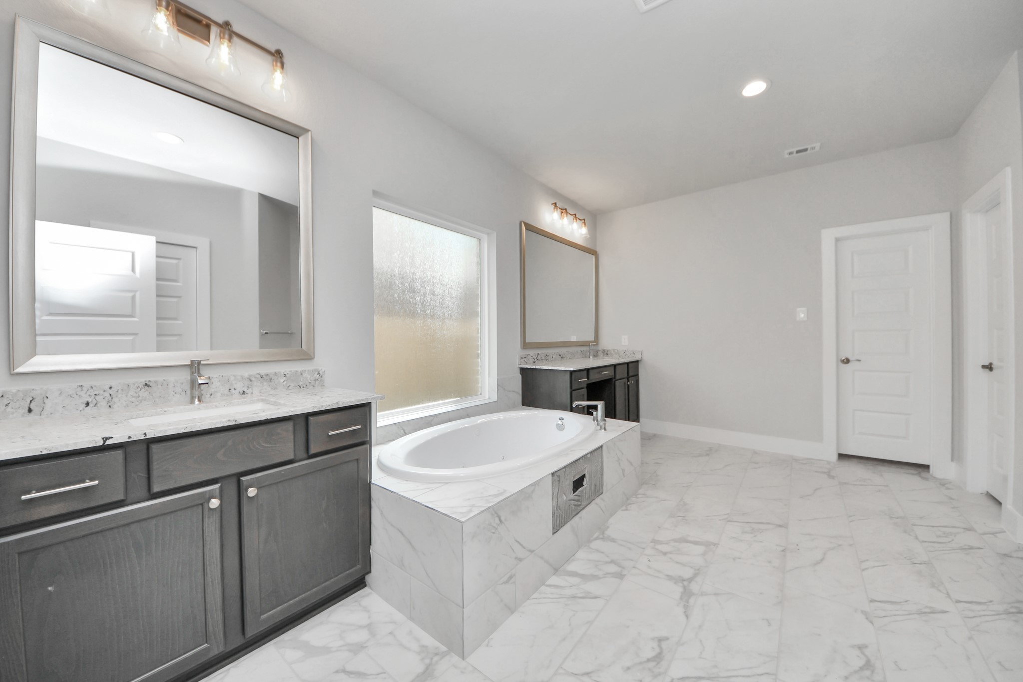 Escape to a spa-like oasis in this primary bathroom. Enjoy a walk-in shower with tile surround, a separate garden tub with custom detailing, and an elegant vanity featuring light countertops, modern hardware, and beautiful vanity lights. Experience luxury and relaxation in every detail. Sample photo of completed home with similar floor plan. Actual colors and selections may vary.