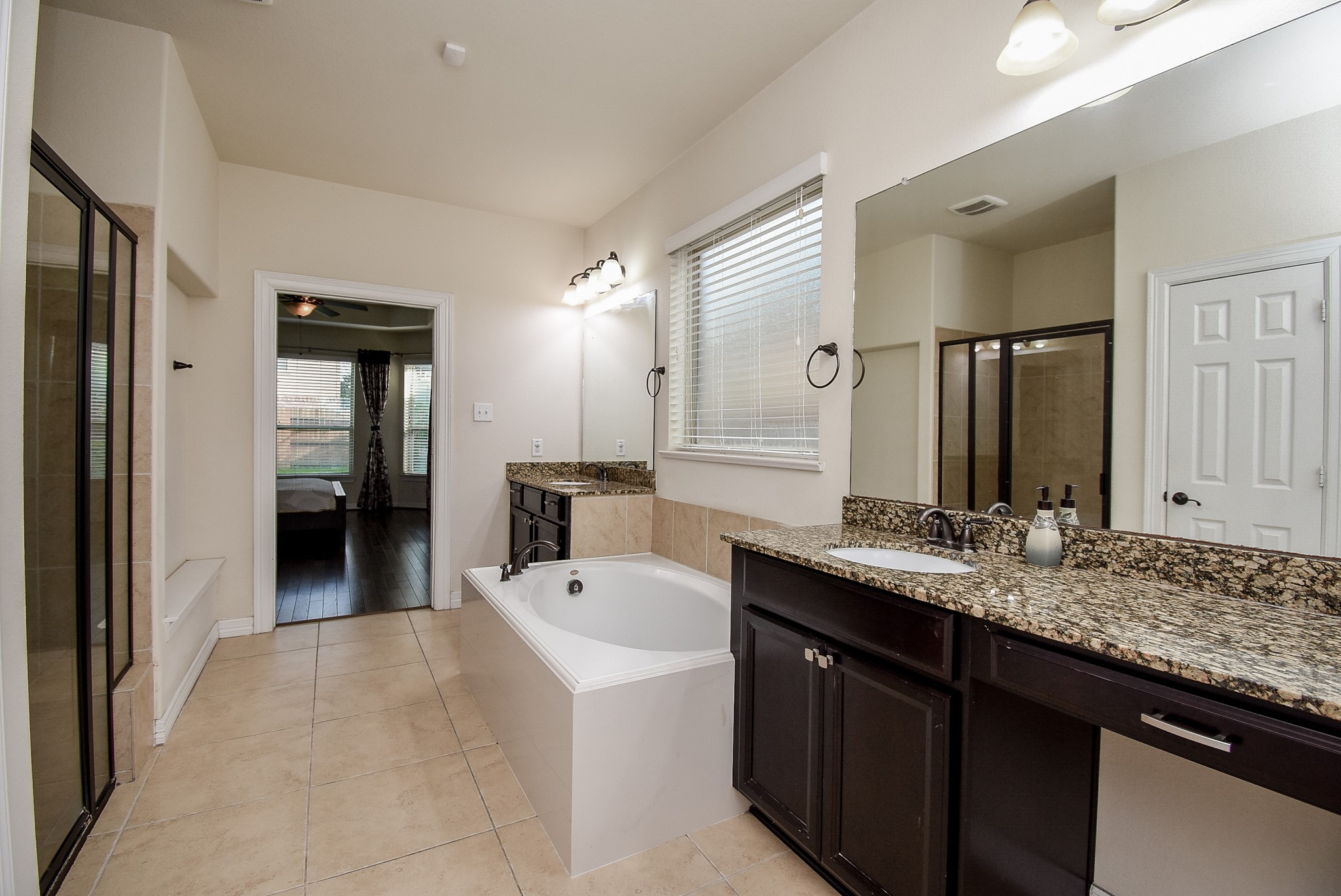 Spacious bathroom with a large soaking tub, granite countertops, dual sinks, and a separate glass-enclosed shower.
