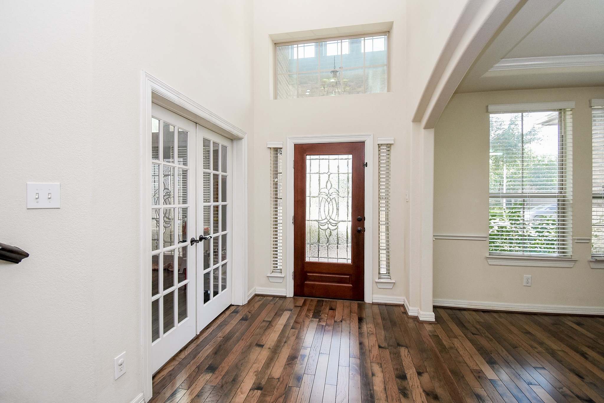 Entryway has high ceilings, featuring a wooden front door with decorative glass, adjacent French doors to the office/study, and large windows providing natural light. Hardwood floors add warmth and elegance.