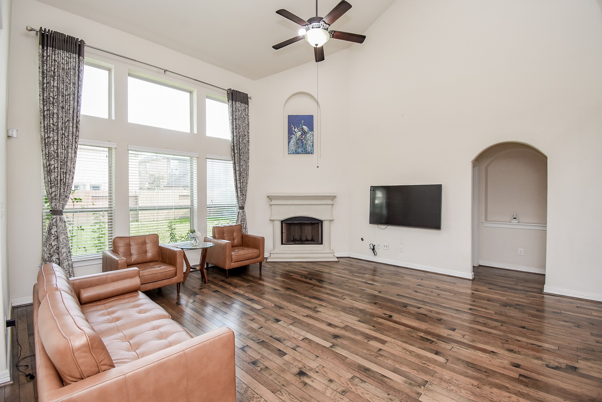 The living room features high ceilings, large windows for ample natural light, and elegant wood flooring. It includes a cozy fireplace as well.