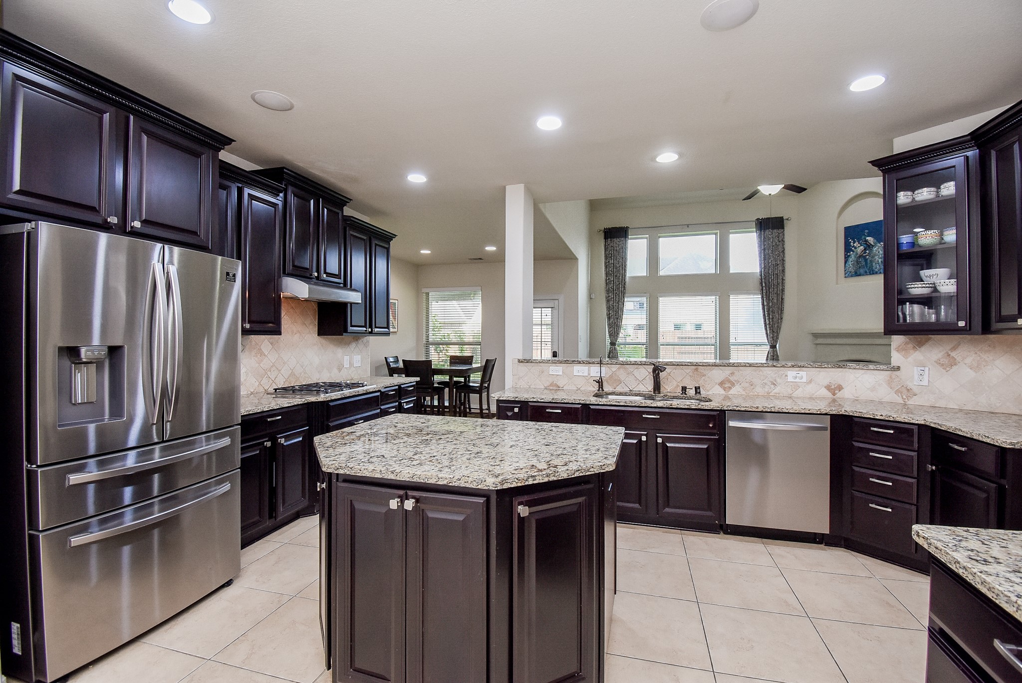 Spacious kitchen features elegant dark wood cabinetry, granite countertops, and modern stainless steel appliances. A central island provides extra workspace.