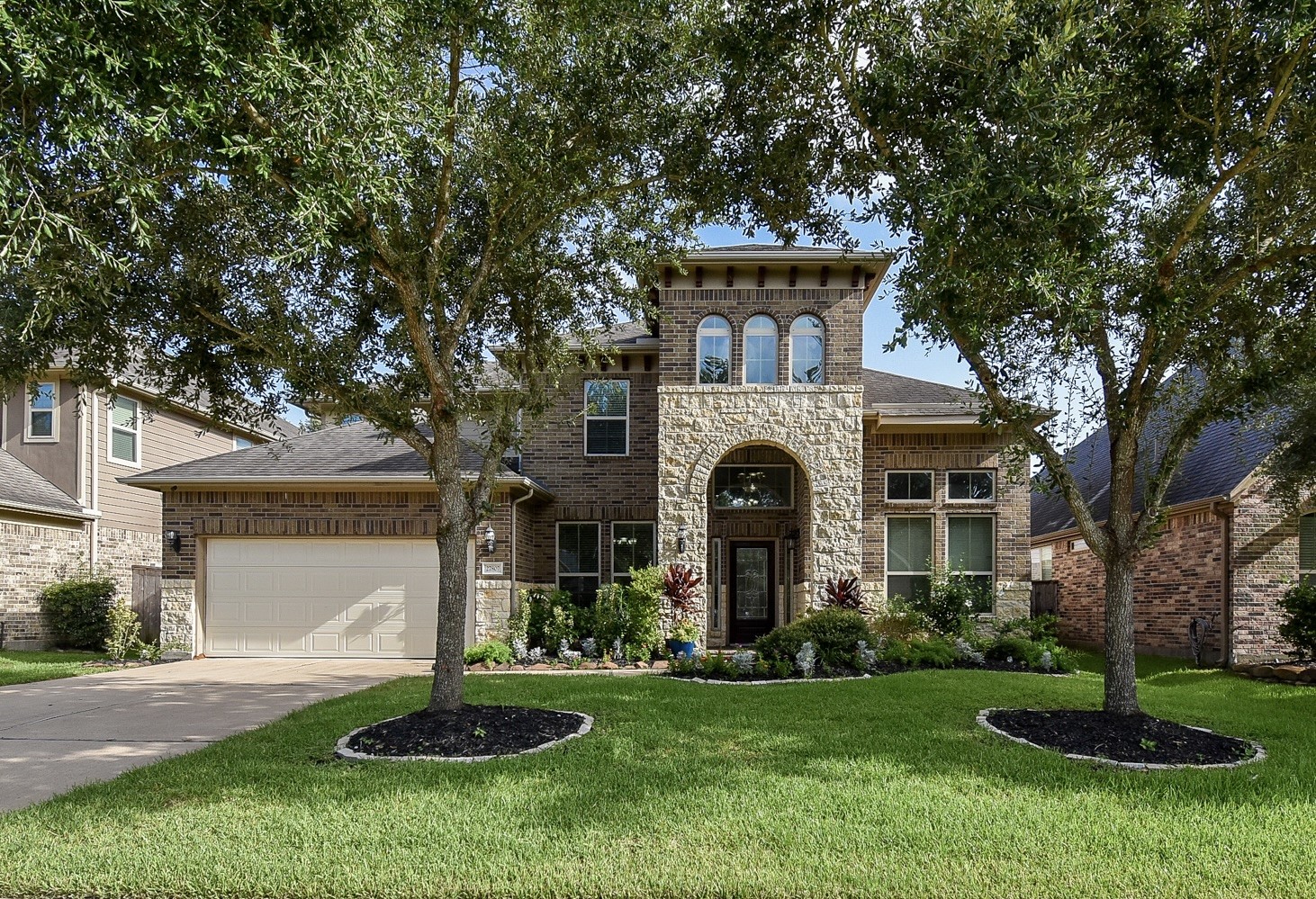A beautiful two-story home with a stone and brick exterior. Features a spacious driveway, and a 3-car garage. The arched entryway adds elegance to the facade.