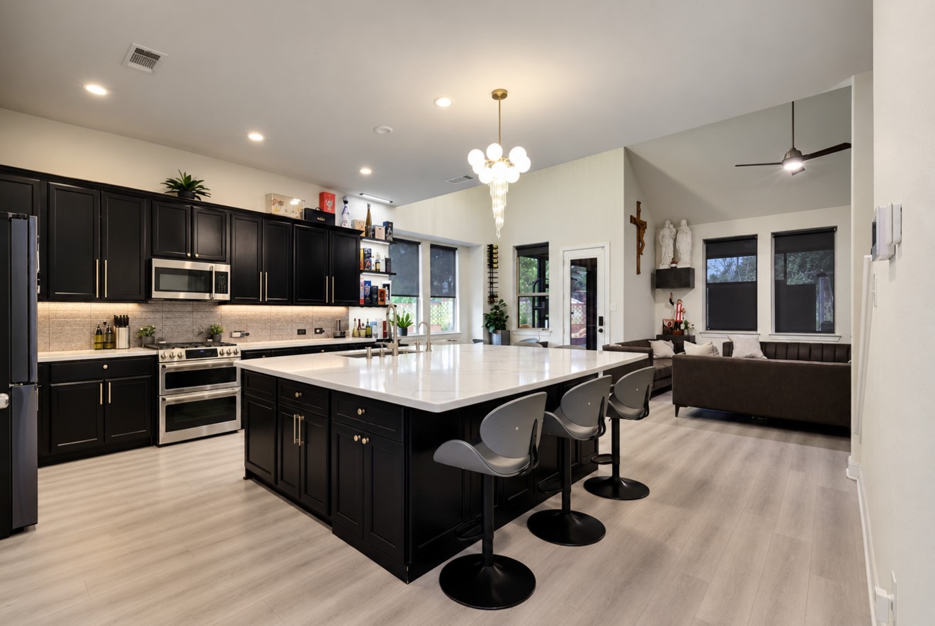 Beautifully updated kitchen featuring a remodeled oversized island with breakfast bar seating, new countertops, and new appliances. Rich dark cabinetry with hardware, under-cabinet lighting, and a statement light fixture creates a stylish space that opens to the main living areaideal for everyday living and entertaining.