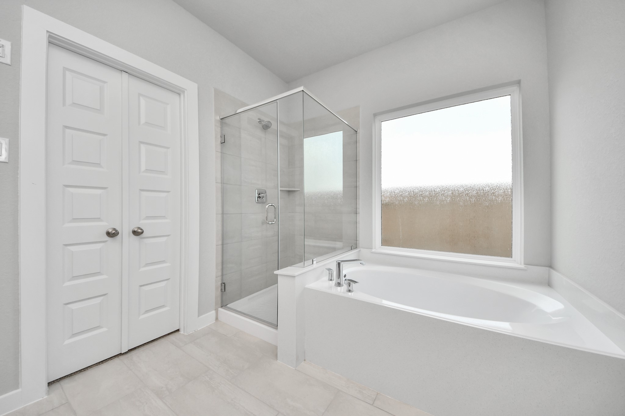 Indulge in a spa-like retreat within the confines of this primary bathroom. Delight in a spacious walk-in shower enveloped in stylish tile surround, unwind in a separate garden tub adorned with custom detailing. Sample photo of completed home with similar floor plan. Actual colors and selections may vary.