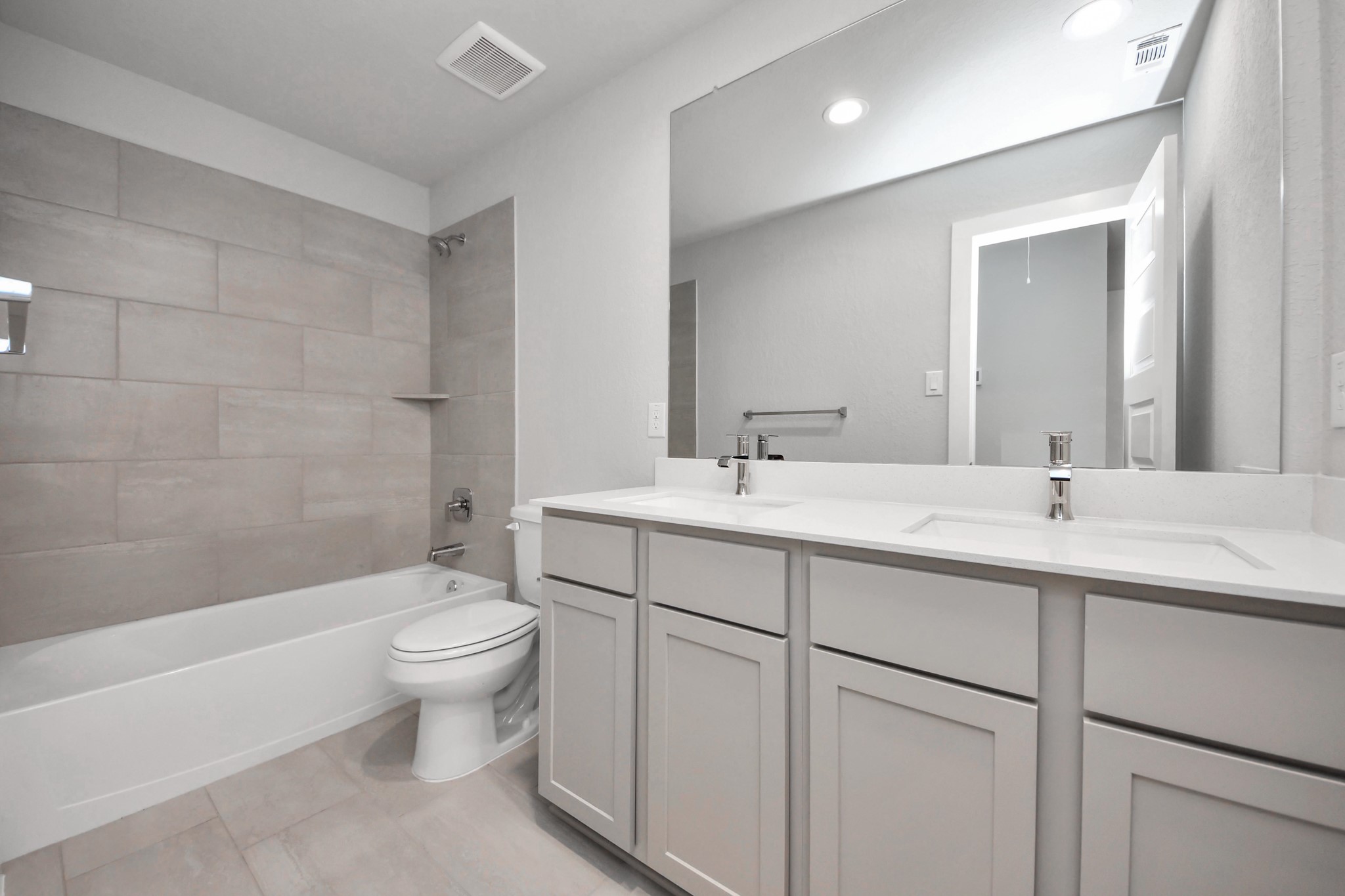 Secondary bath features tile flooring, bath/shower combo with tile surround, light stained wood cabinets, beautiful light countertop. Sample photo of completed home with similar floor plan. Actual colors and selections may vary.