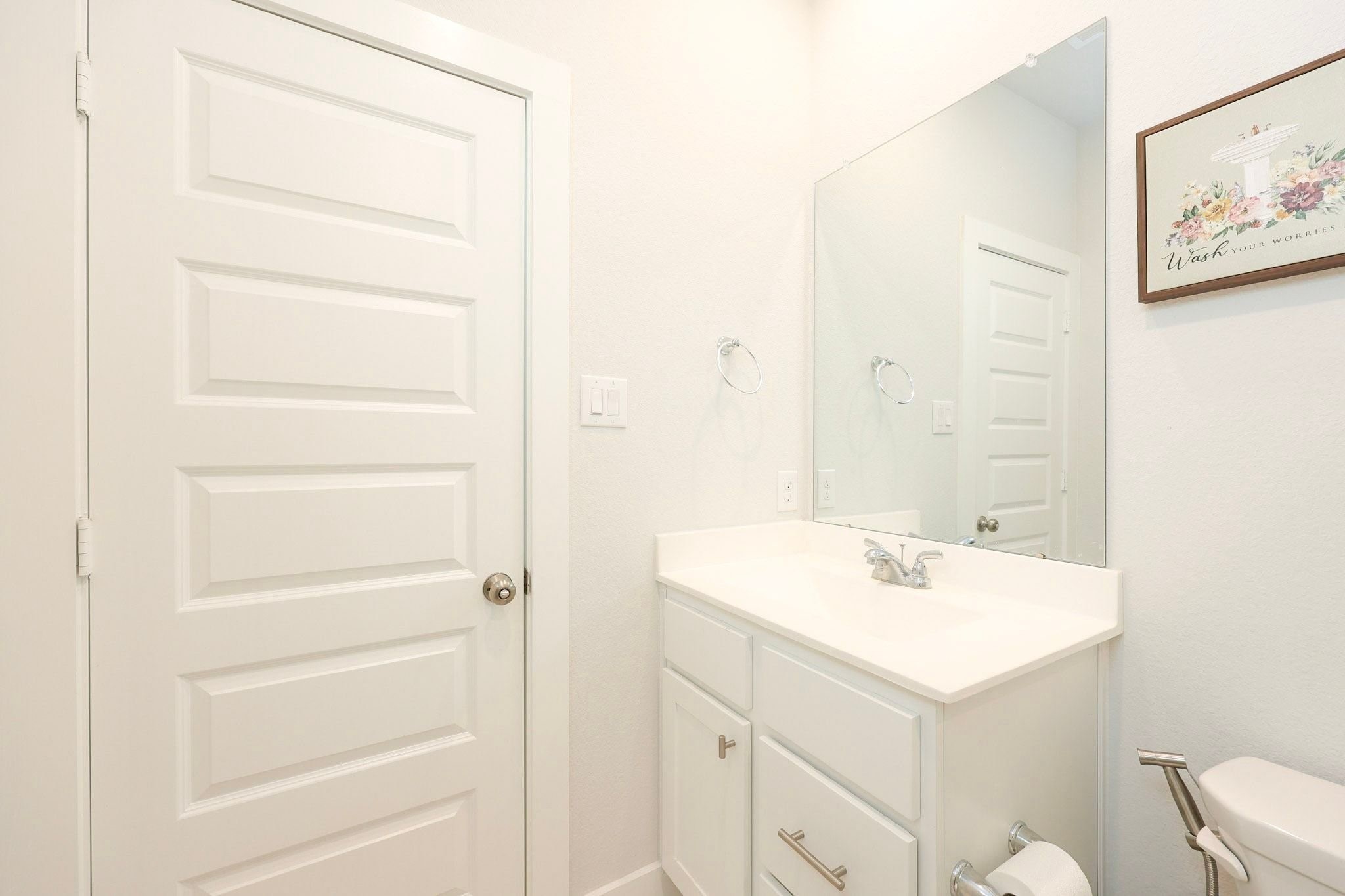 Secondary bathroom on first floor situated across from secondary bedroom with a sleek vanity, large mirror, and fresh white finishes creating a clean and inviting atmosphere.