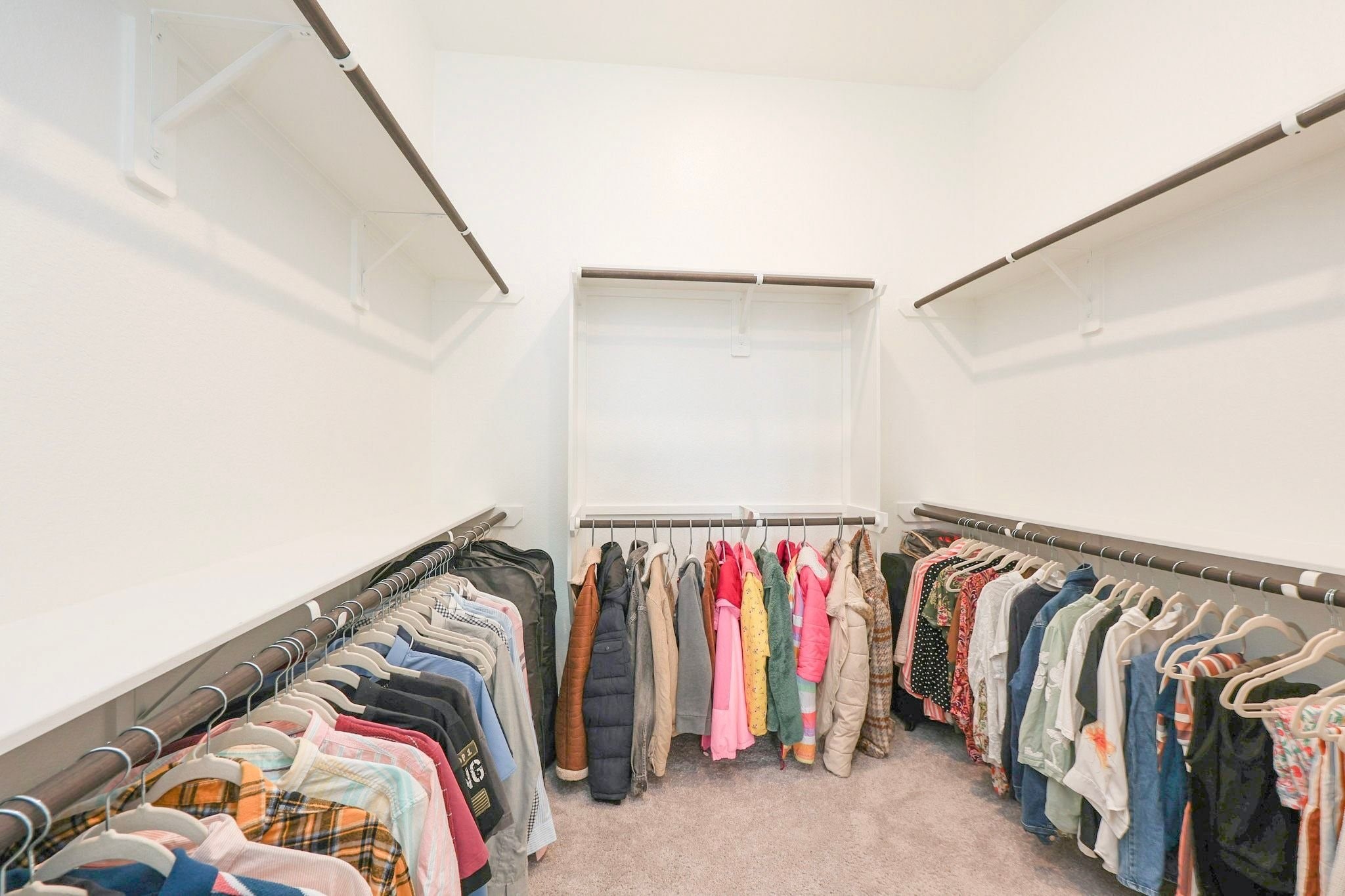 Spacious primary walk-in closet with ample hanging space and shelving, perfect for organized storage.
