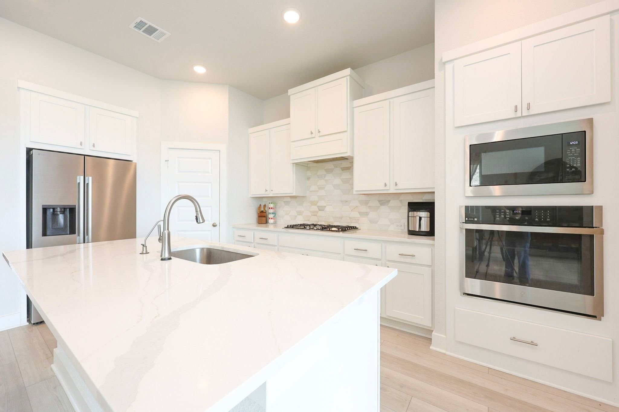 Open kitchen featuring a spacious quartz island, stainless steel appliances, and ample white cabinetry for storage.