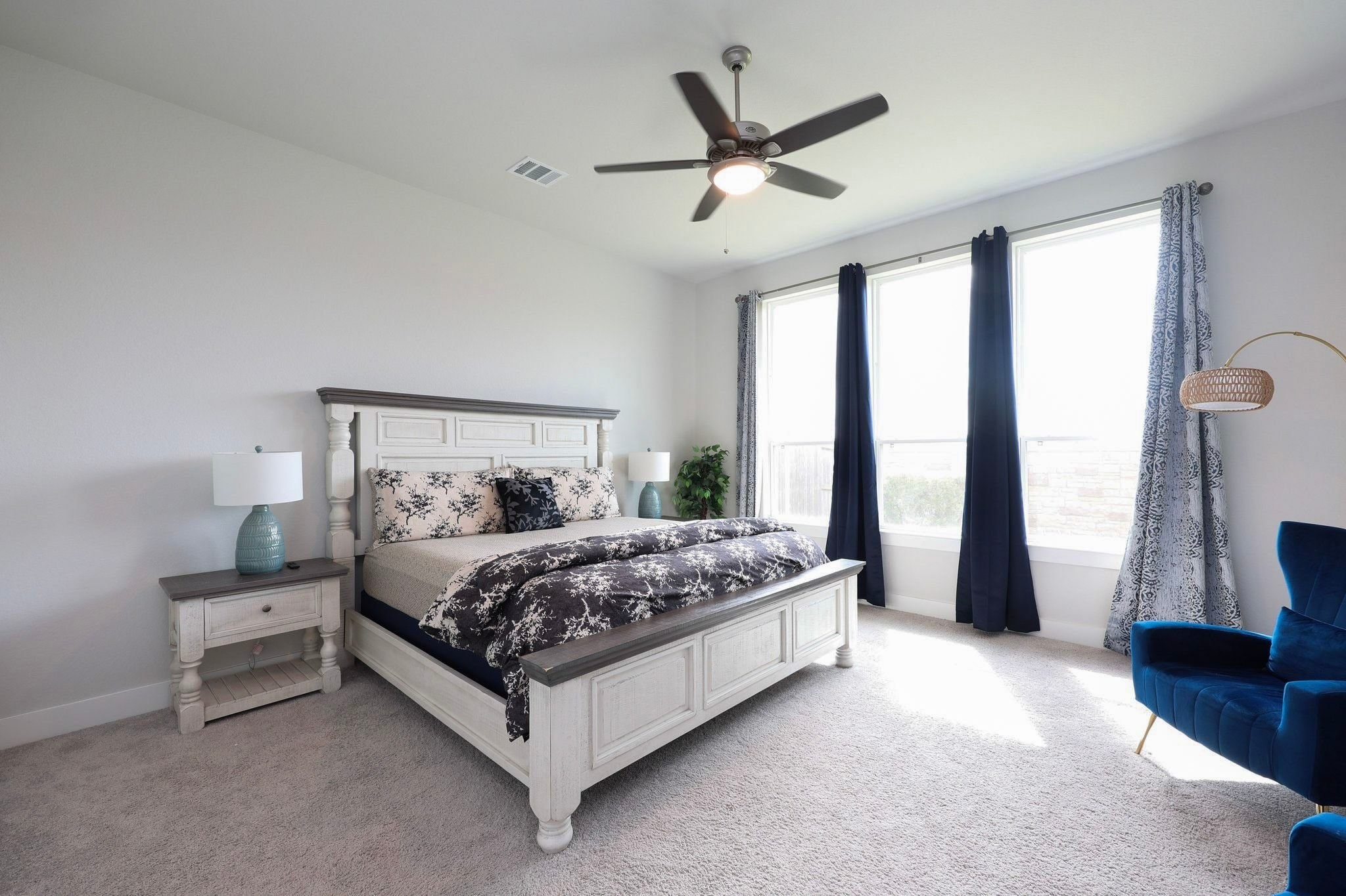 Spacious and bright primary bedroom with floor to ceiling windows, featuring a ceiling fan, elegant window coverings, and plush carpet.