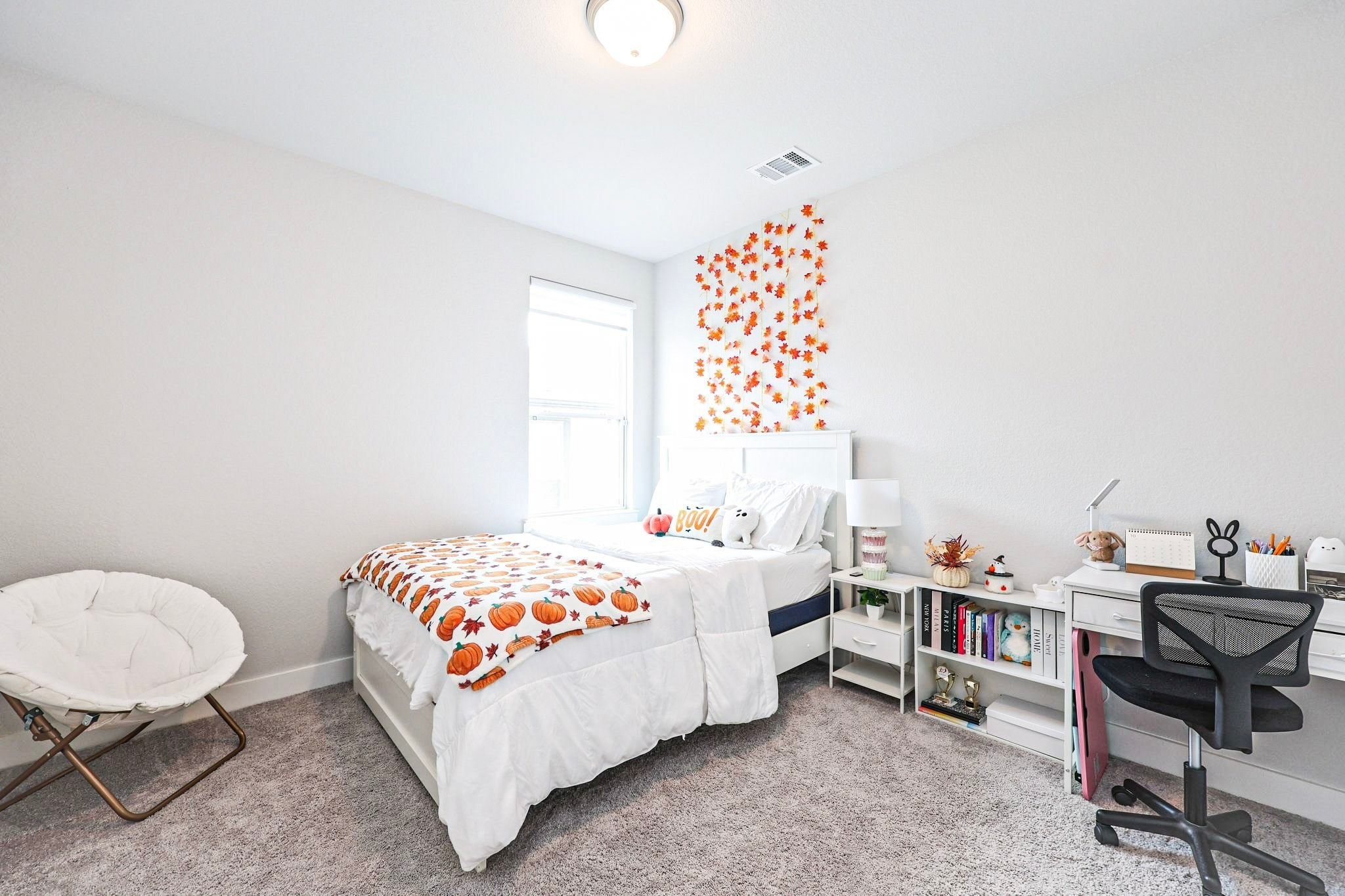 Third bedroom upstairs with one large window features a comfortable bed with playful decor, a functional desk space, and soft carpet flooring, perfect for relaxation and productivity. The room is spacious.
