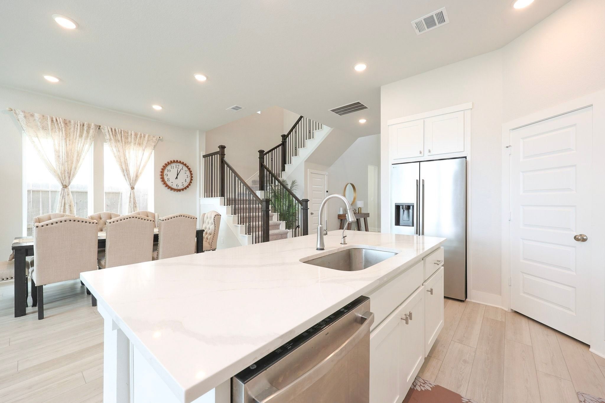The spacious kitchen features a pantry and a dedicated refrigerator alcove. An elegant staircase with black iron balusters creates a grand and inviting entrance.