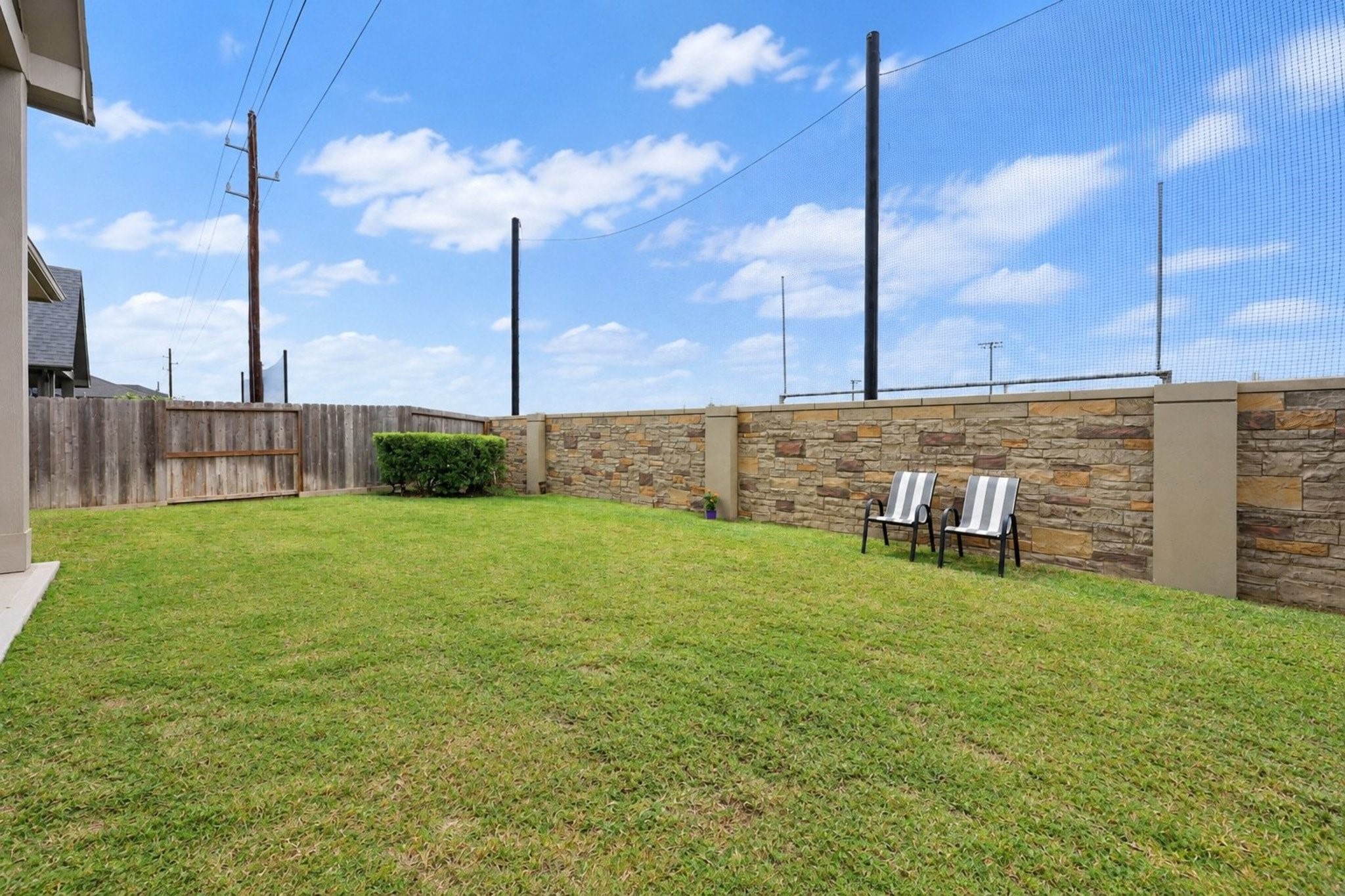 Spacious backyard with lush green lawn, privacy fencing, and a charming stone wall, perfect for relaxation or outdoor activities.