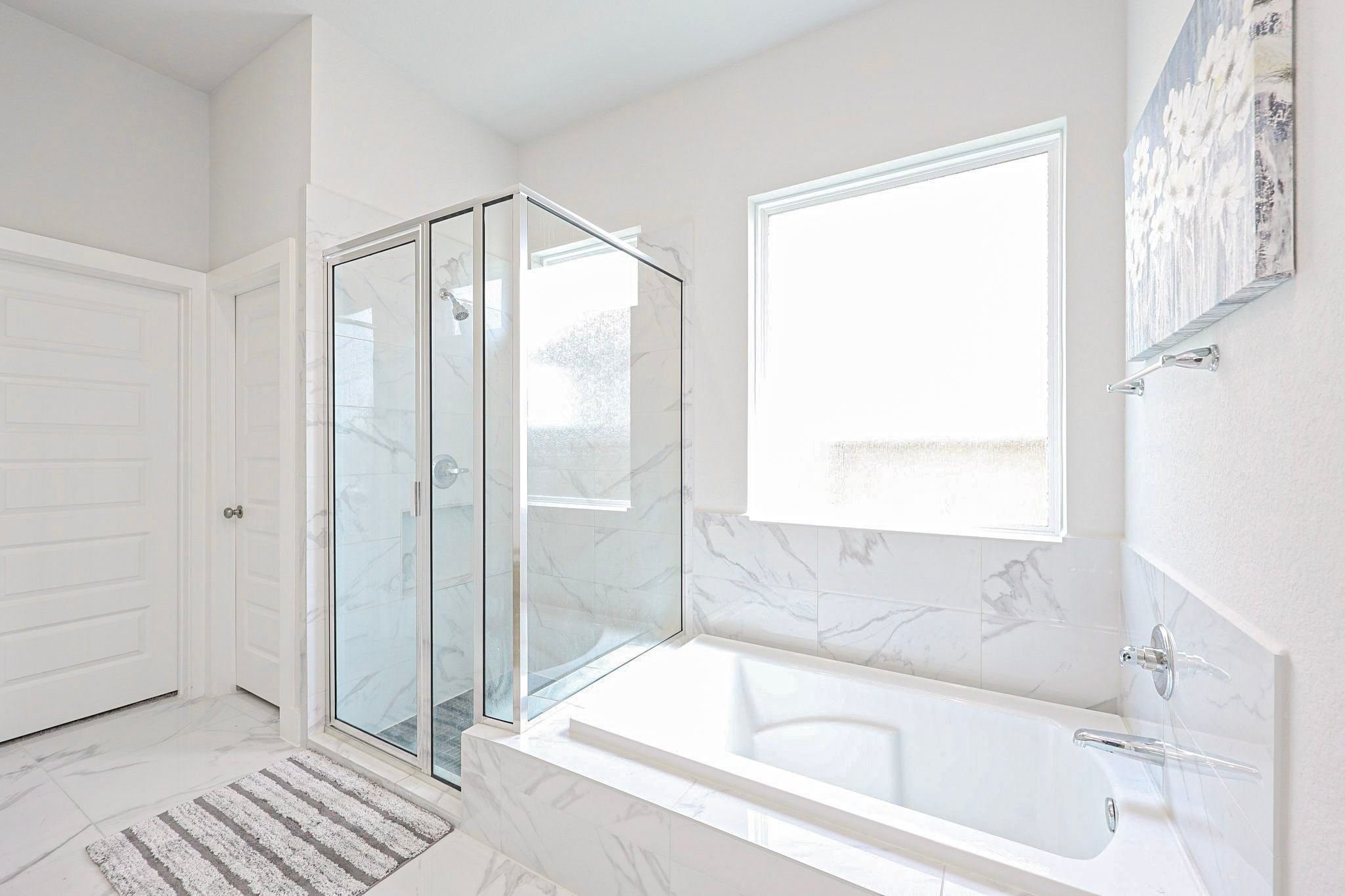 Elegant primary bathroom on first floor featuring a glass-enclosed shower and a luxurious soaking tub, accented with modern marble tiles and abundant natural light.