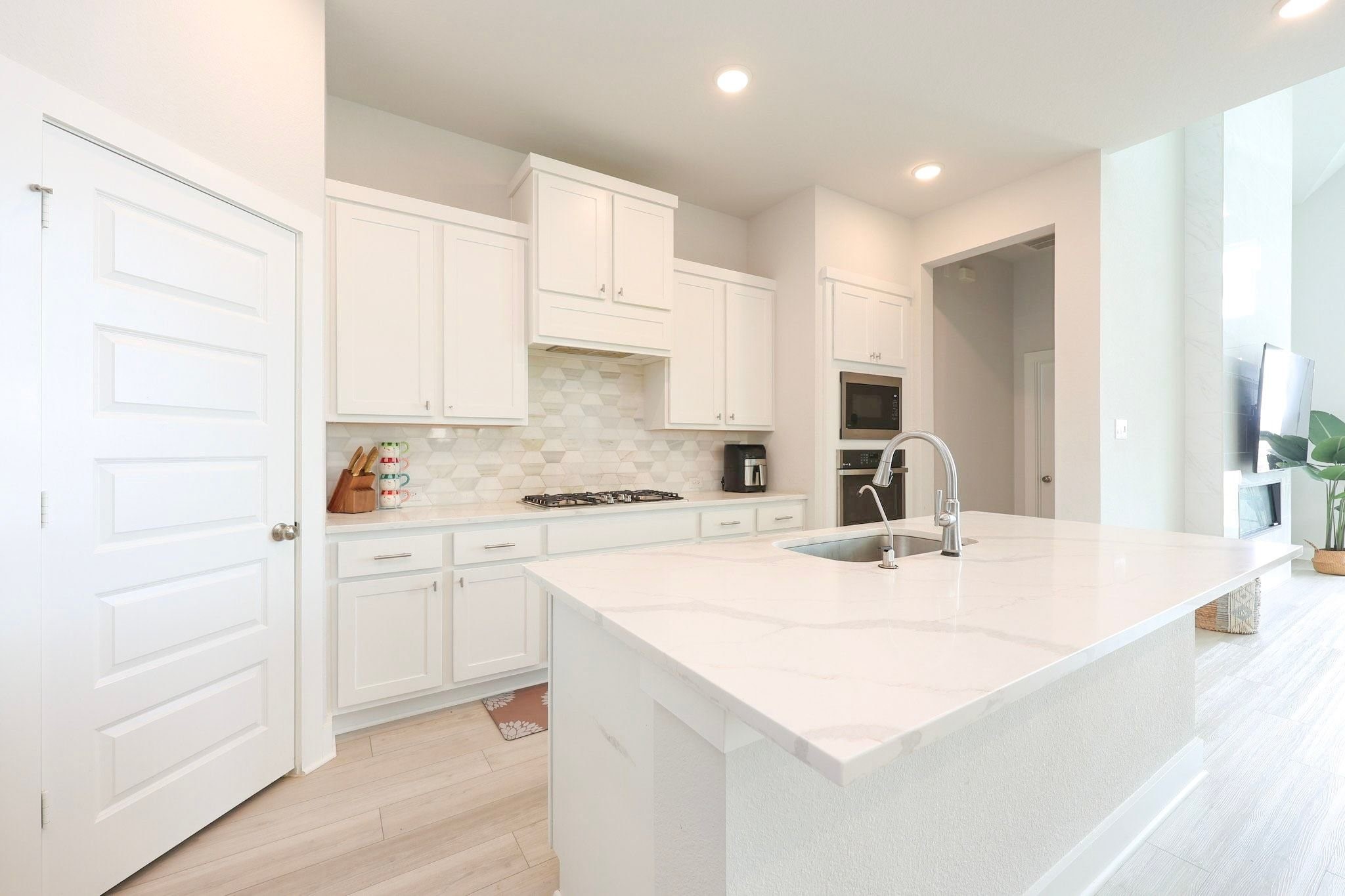 Modern kitchen featuring sleek white cabinetry, a spacious quartz island with a built-in sink, and stylish backsplash, perfect for culinary enthusiasts.