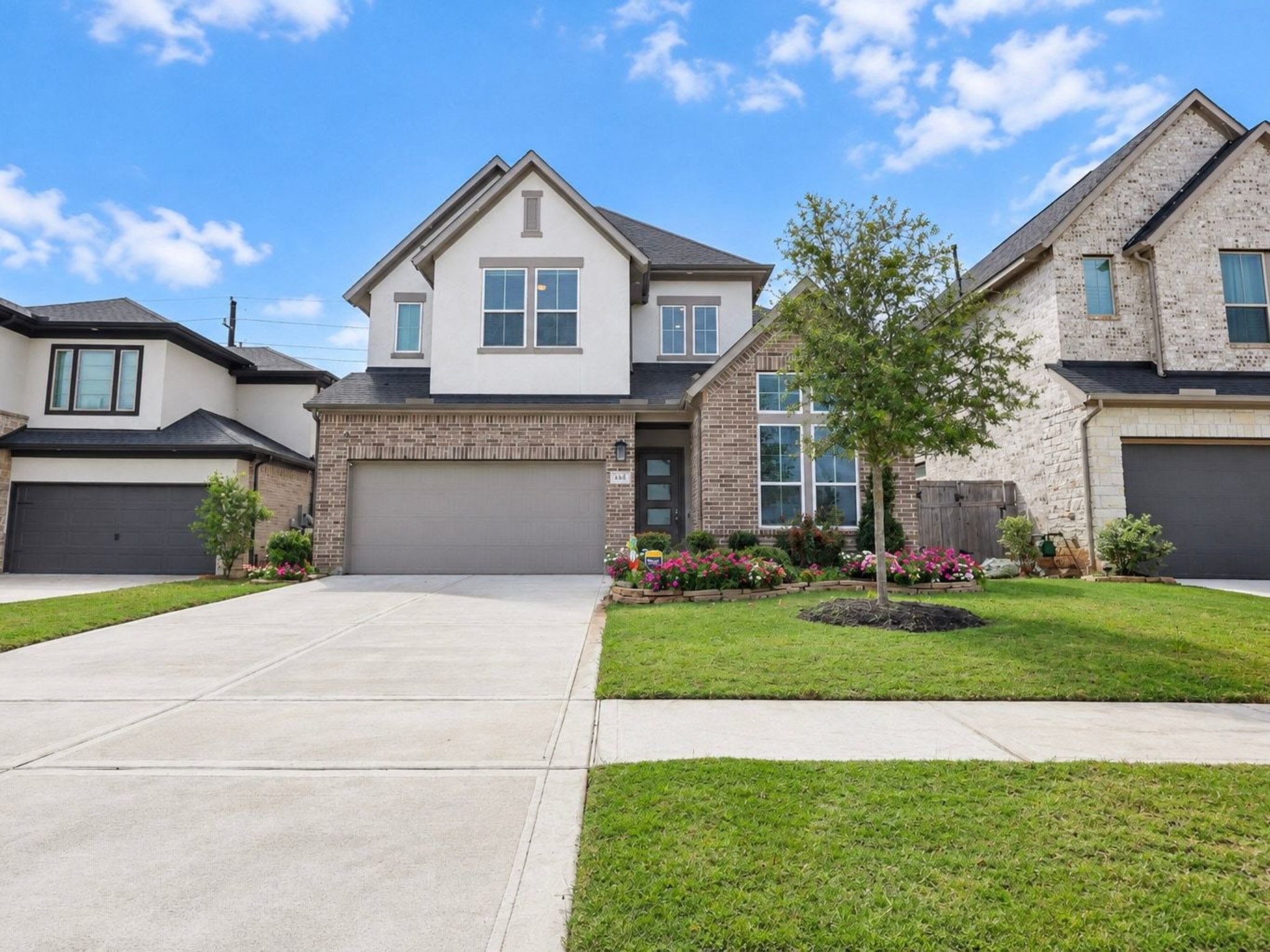 Charming two-story home with a brick and stuco facade and modern design, featuring a spacious driveway, manicured lawn, and inviting landscaped garden.