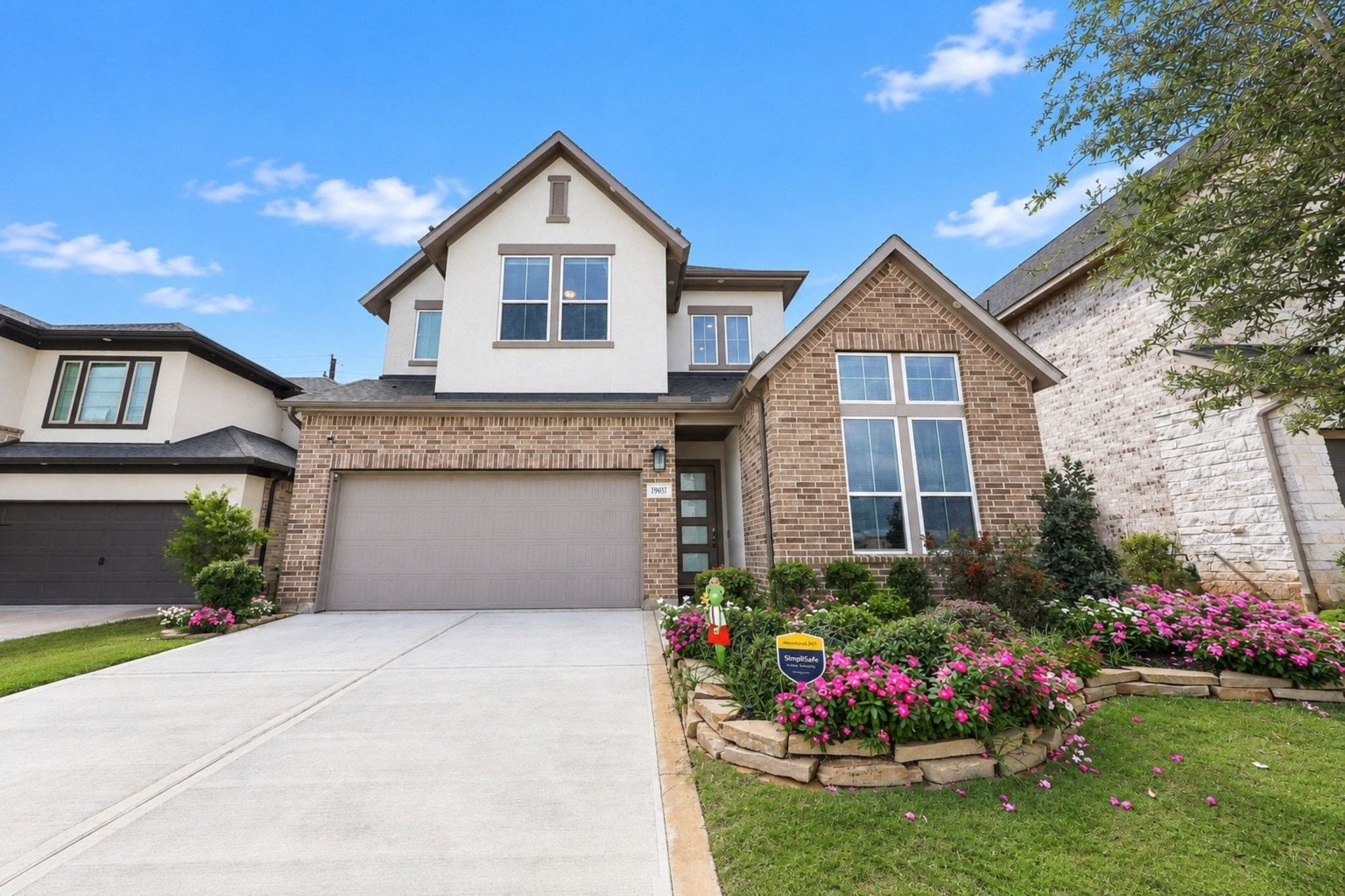 Beautiful two-story home featuring a modern brick & stucco facade, clerestory windows, and a beautifully landscaped front yard with vibrant flowers.