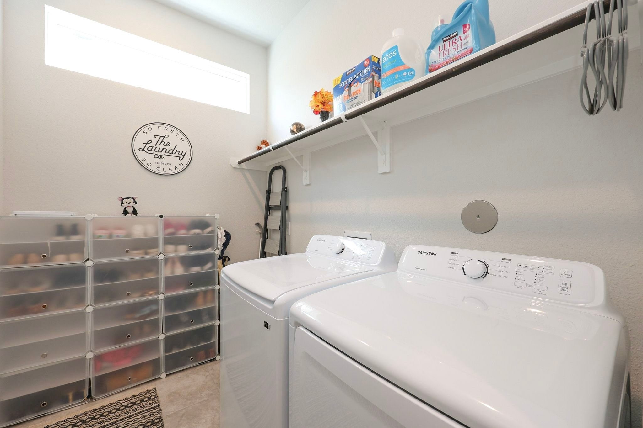 Bright and organized laundry room on 1st floor featuring modern appliances, ample shelving for storage, and natural light from a high window.