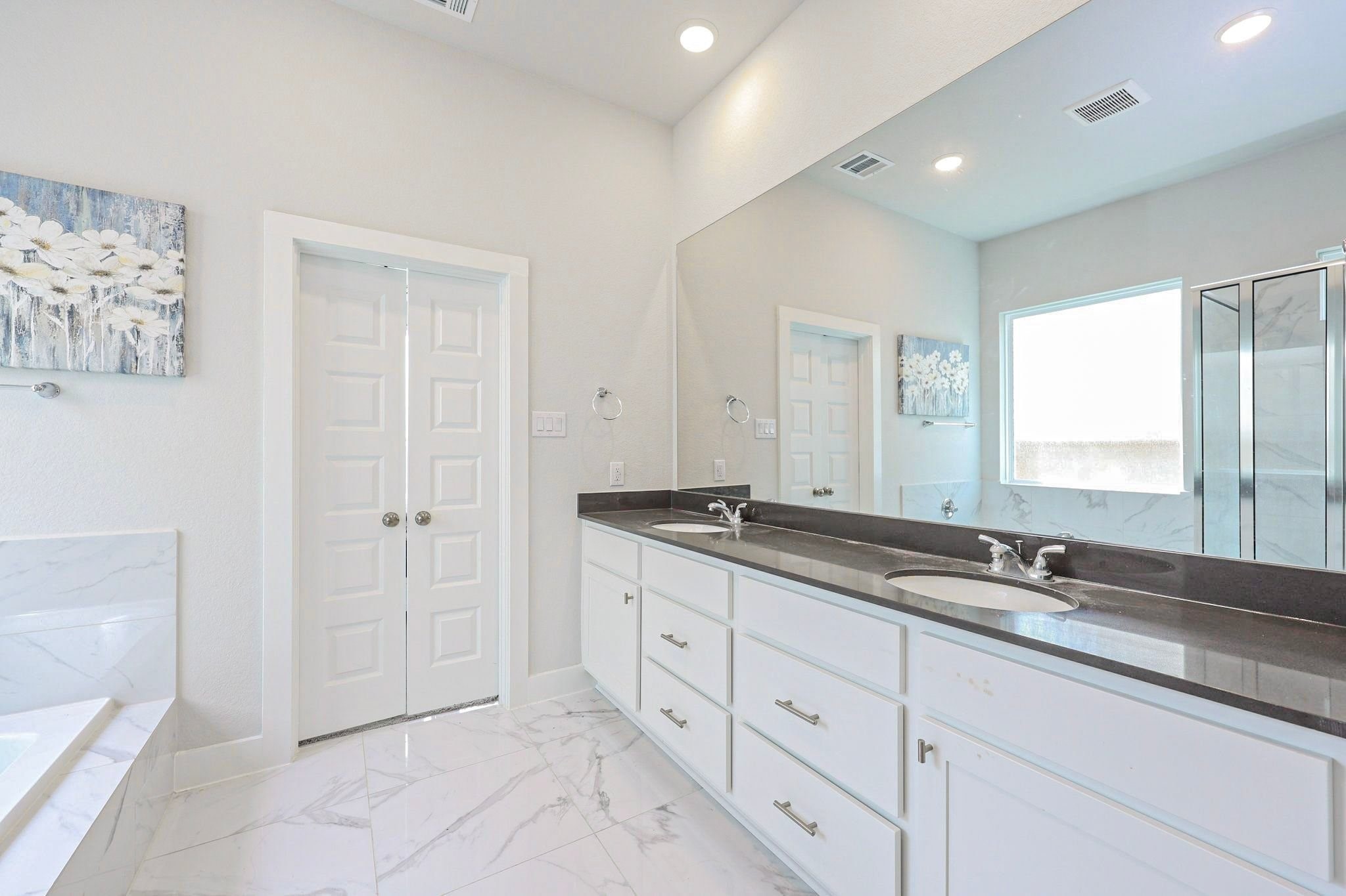 Luxurious primary bathroom with dual sinks, elegant marble flooring, and a spacious glass-enclosed shower.