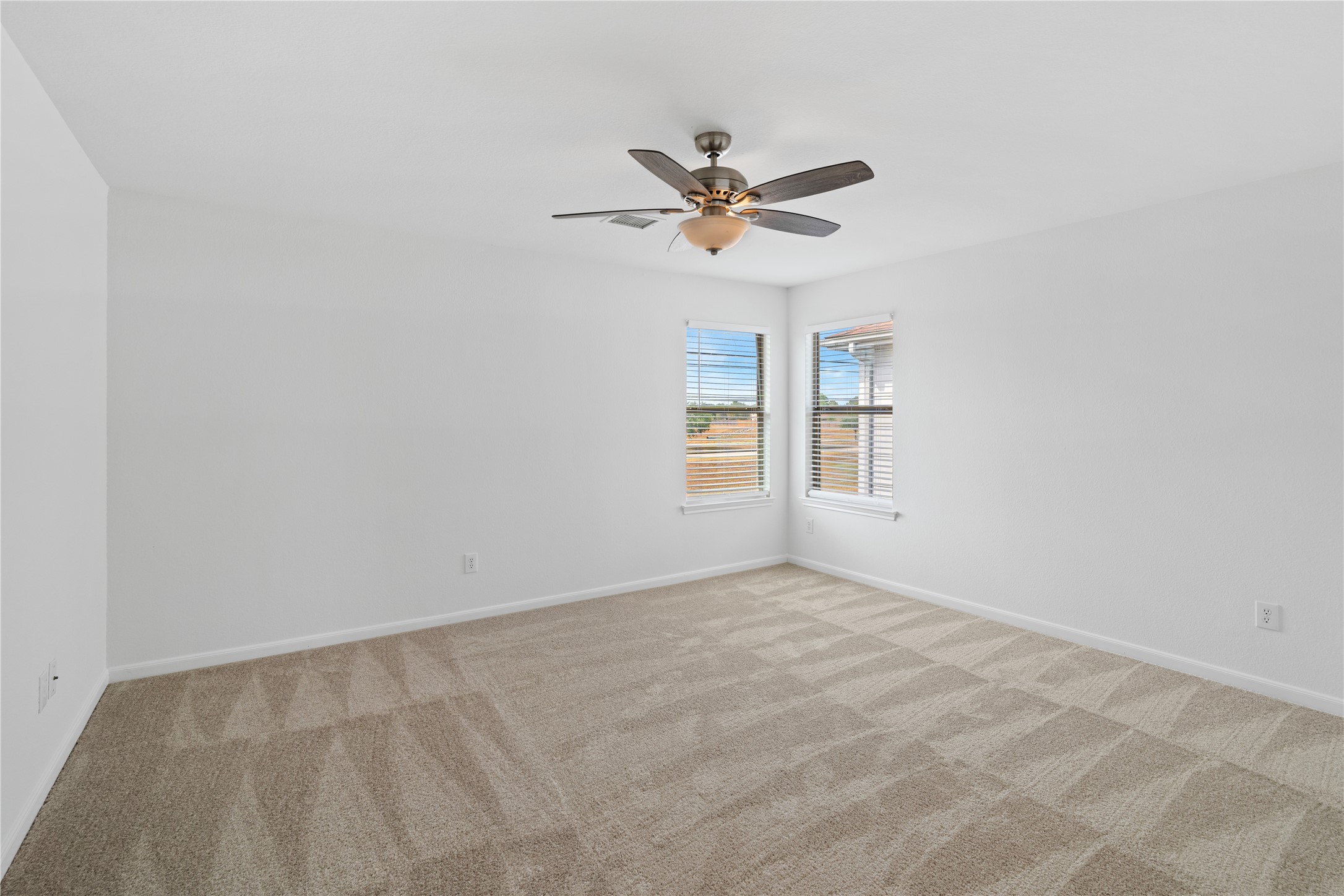 Bedroom  Spacious carpeted bedroom with crisp neutral finishes, a ceiling fan, and two windows providing abundant natural light.