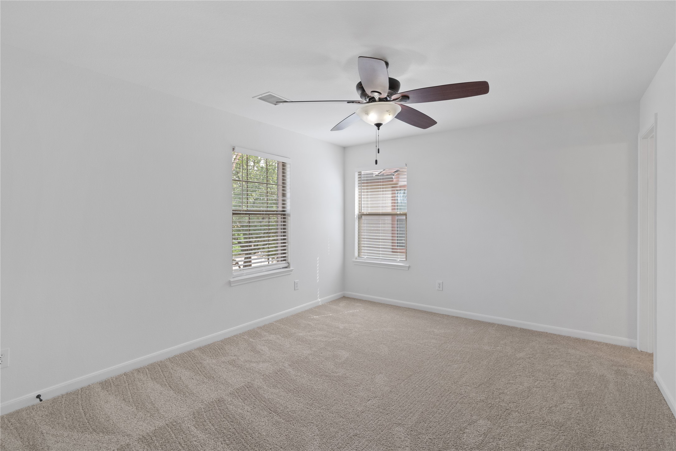Bedroom  Generously sized carpeted bedroom with two windows, a ceiling fan, and a bright neutral color palette.