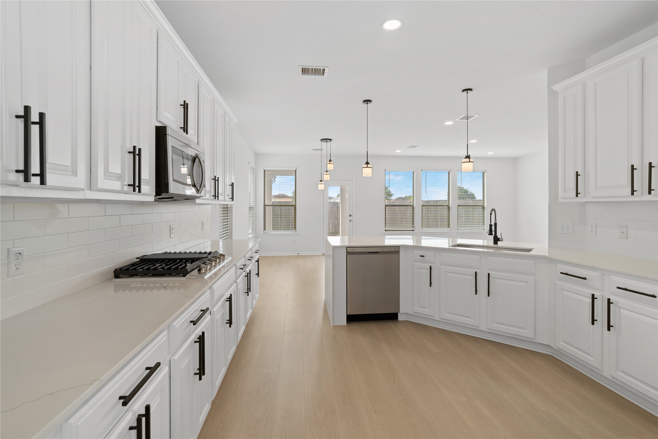 Kitchen  Spacious kitchen features extensive cabinetry and counter space, stainless steel dishwasher, peninsula with sink, modern black fixtures, and an open sightline into the adjoining living and dining areas.