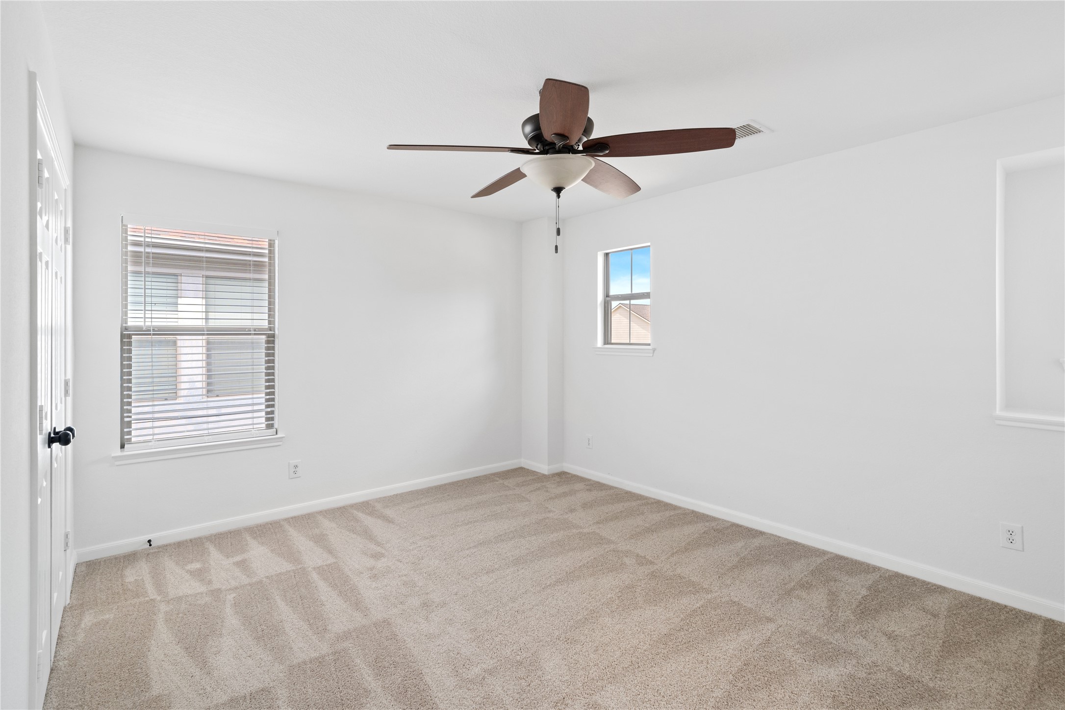 Bedroom  Bright secondary bedroom featuring neutral carpet, a ceiling fan, and multiple windows for natural light.