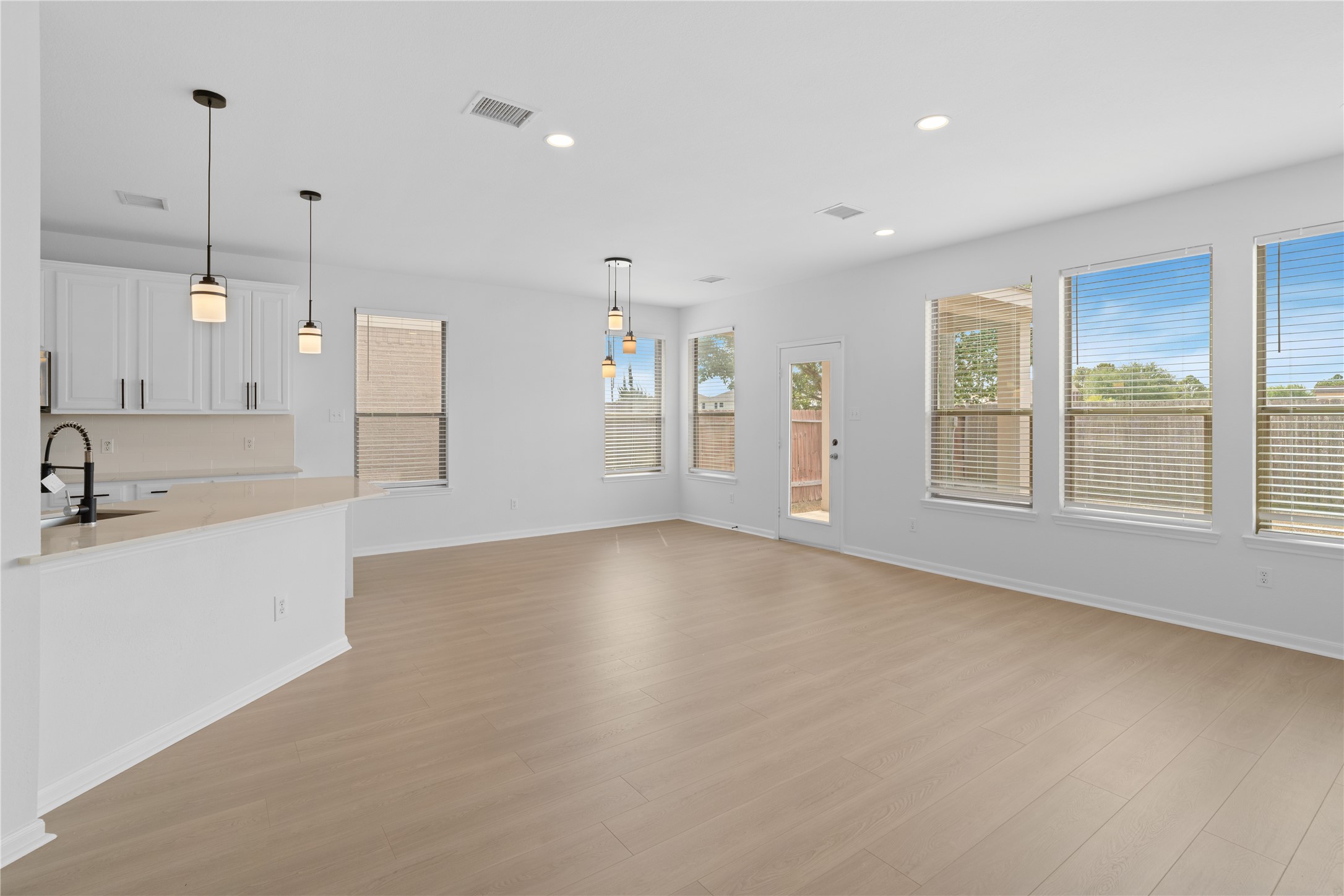 Open-Concept Living & Dining Area  Bright, open living and dining space features light-toned flooring, recessed lighting, contemporary pendant fixtures, and an abundance of windows. The open layout creates an easy connection between the kitchen and gathering areas.