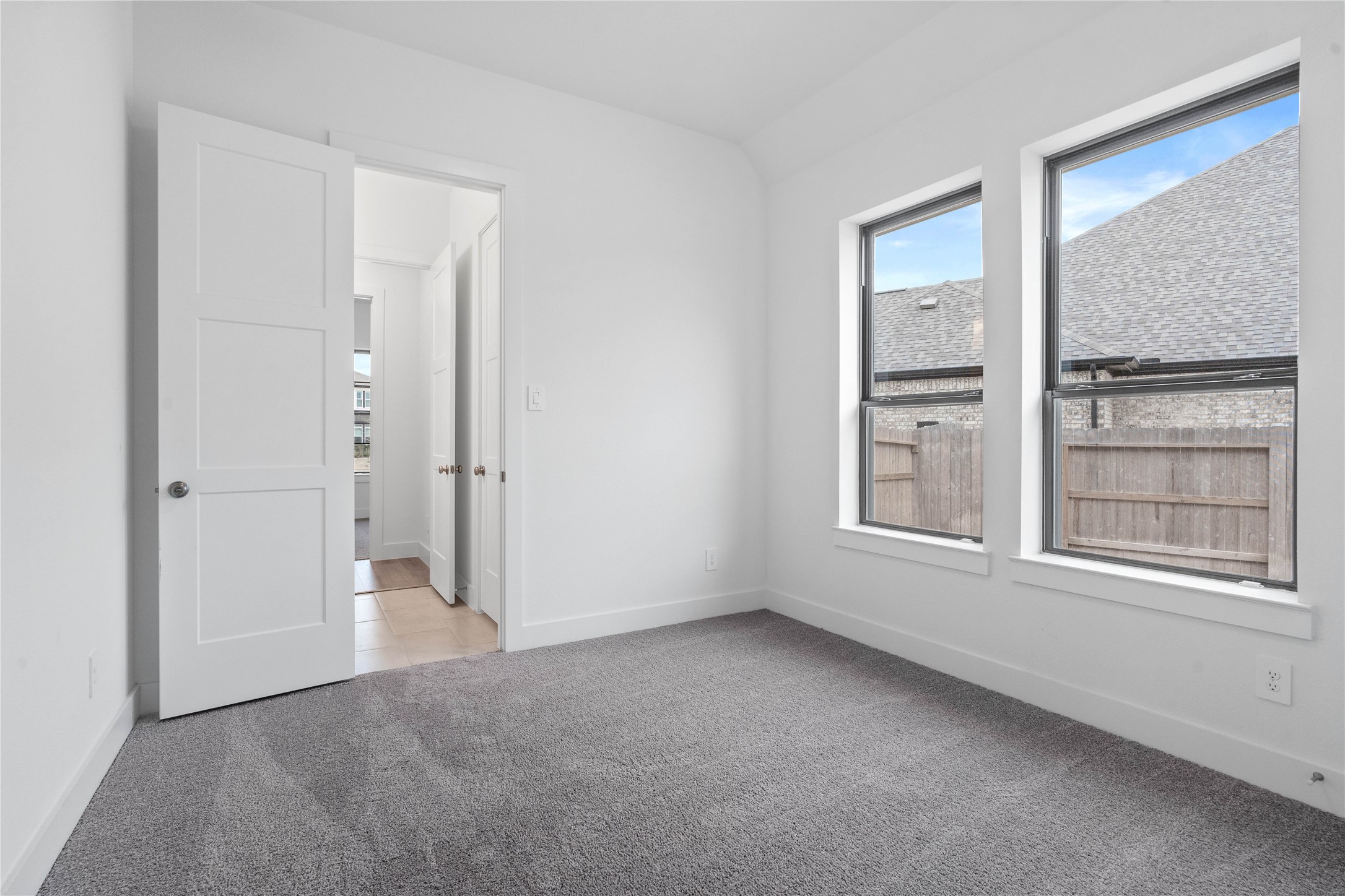 This secondary bedroom features plush carpet flooring, neutral tone walls, two large windows, an access door to a shared secondary bathroom.