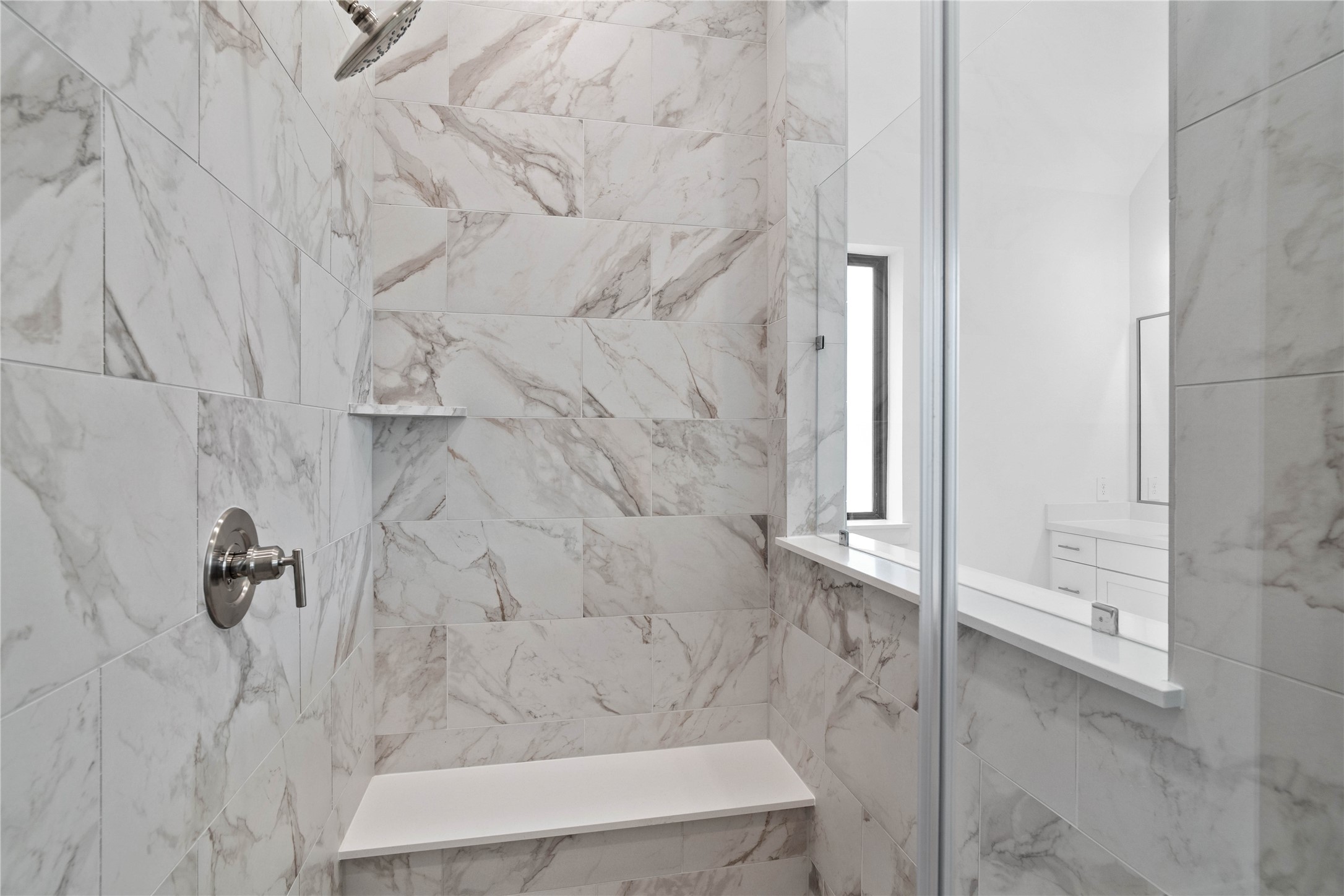 The walk-in shower includes a convenient, integrated bench with a niche shelf, offering comfort, extra storage space, and a high-end, custom appearance.