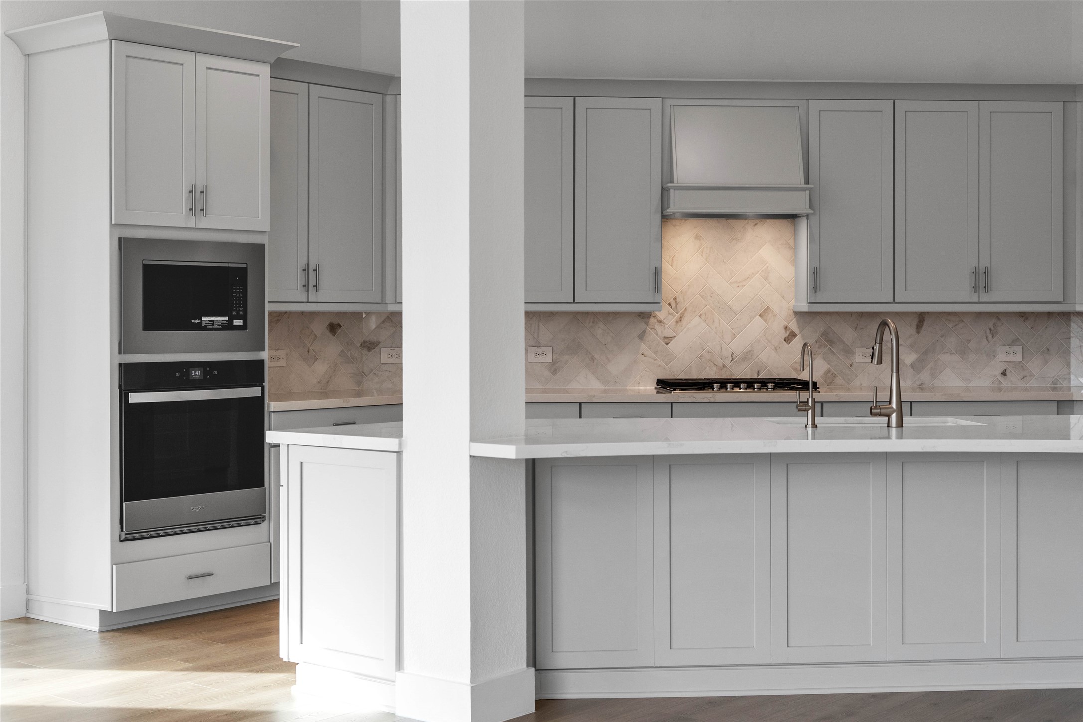 The stunning herringbone tile backsplash serves as a sophisticated focal point, featuring subtle marble-like veining that adds texture and visual depth to the space.