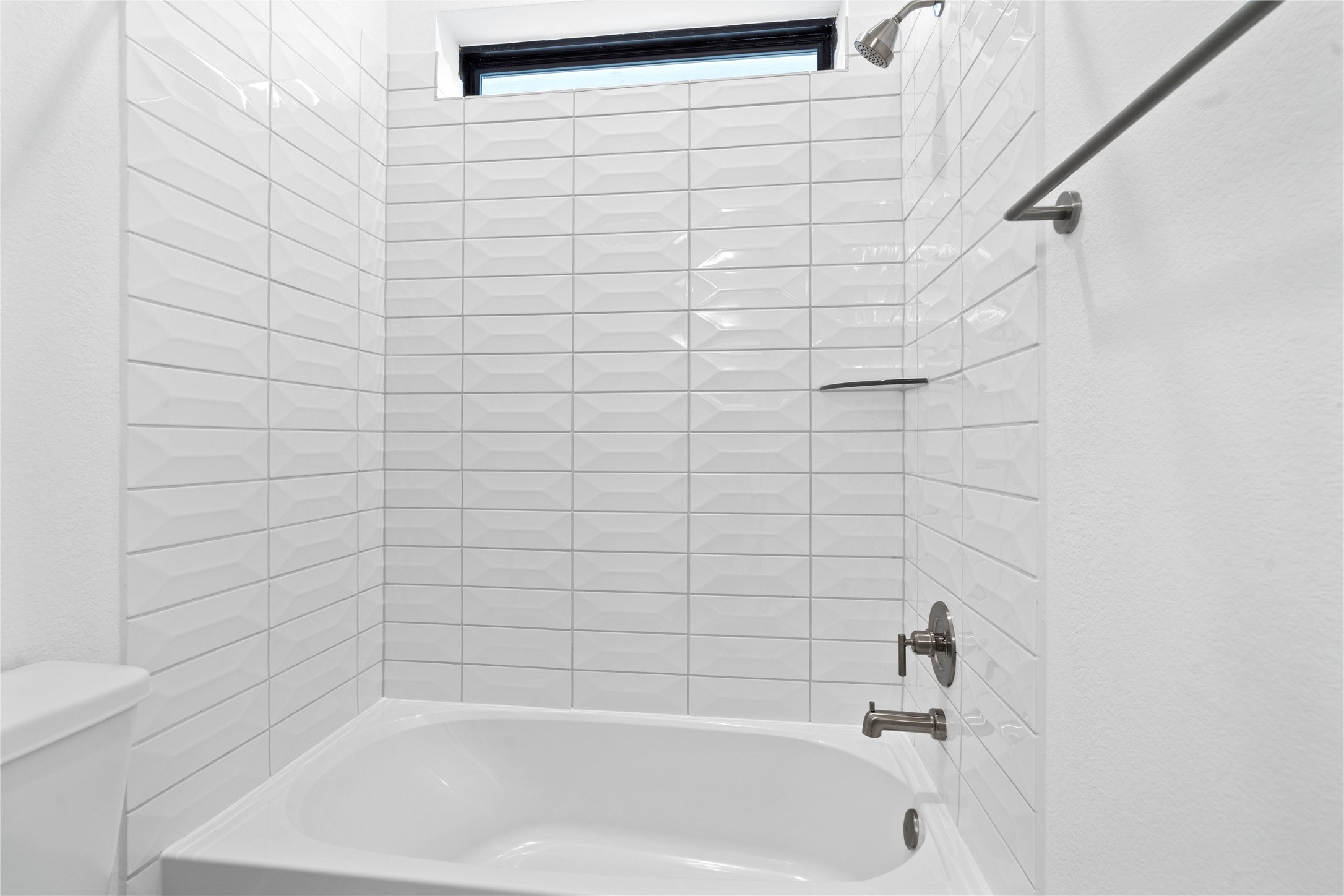 This modern bathroom features a clean white alcove bathtub paired with a sophisticated white subway tile surround that boasts a unique, elongated hexagonal pattern.