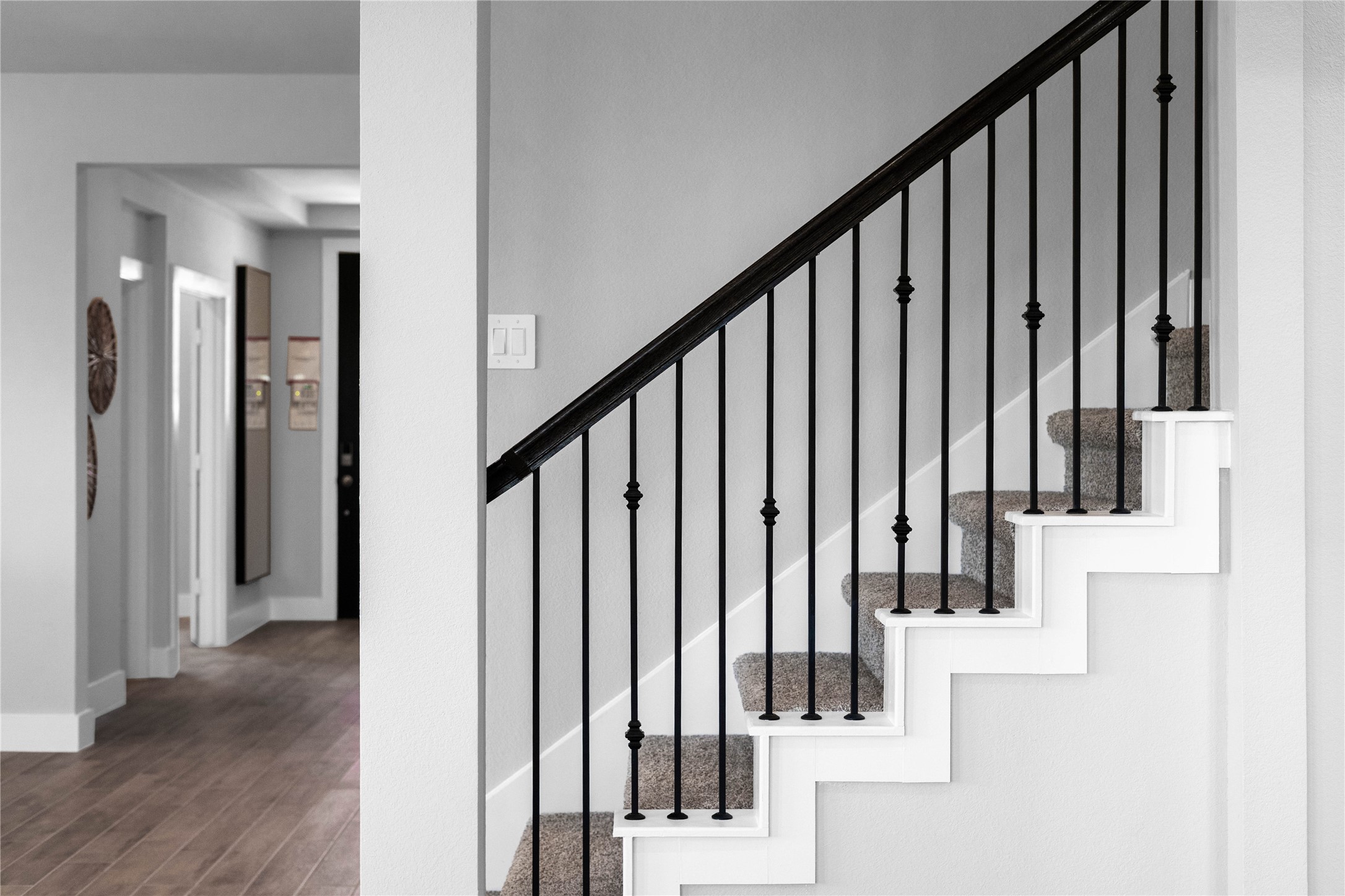 An elegant staircase featuring a modern mix of materials, including sleek black wrought iron balusters with decorative knuckle accents. The clean white risers and plush neutral carpeting create a sophisticated, high-contrast look that perfectly complements the home's contemporary aesthetic