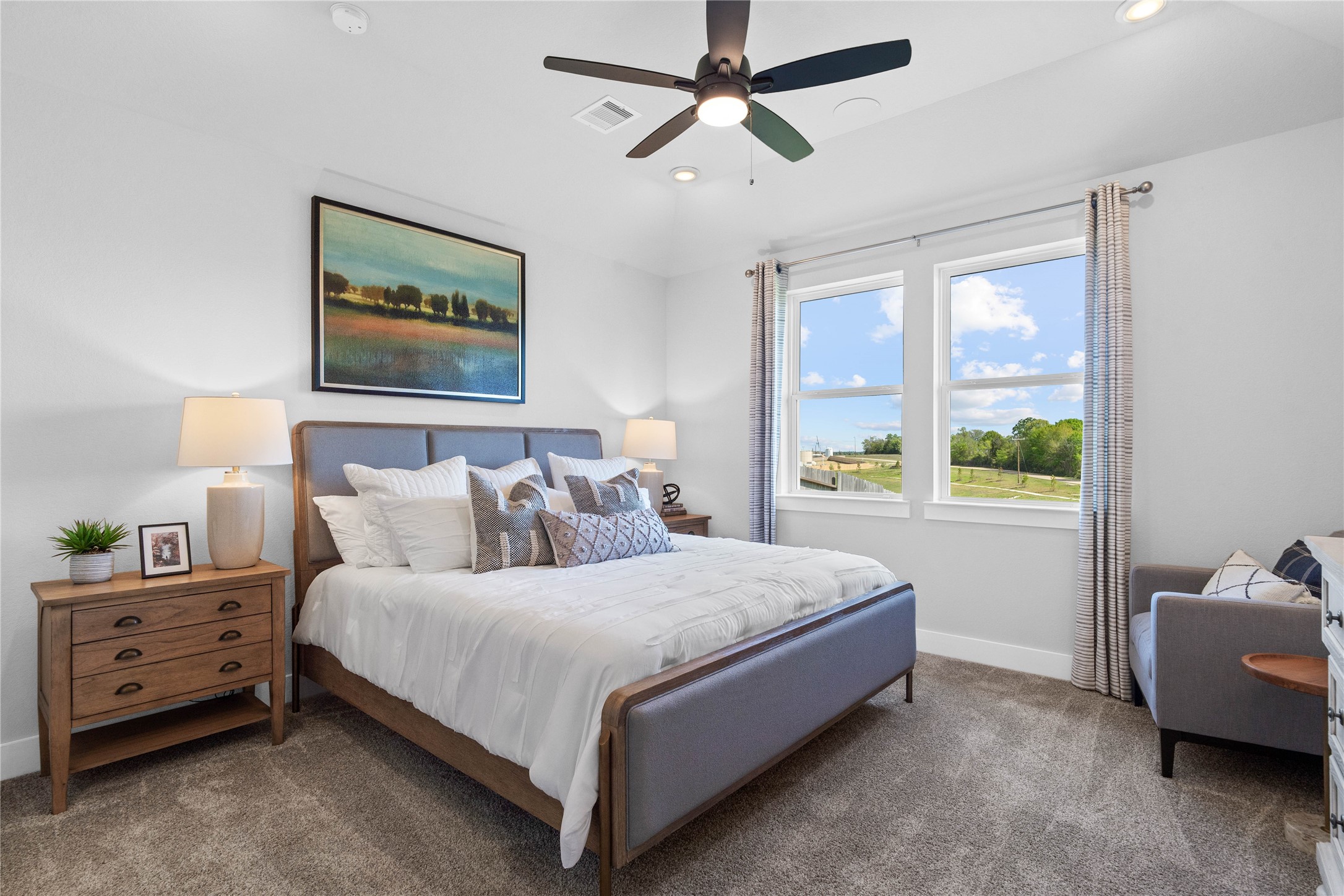 The primary bedroom provides a peaceful escape with a bright, neutral palette, sloped ceilings, ceiling fan large windows, and plush carpet flooring, creating a calm and restorative atmosphere to end your day.