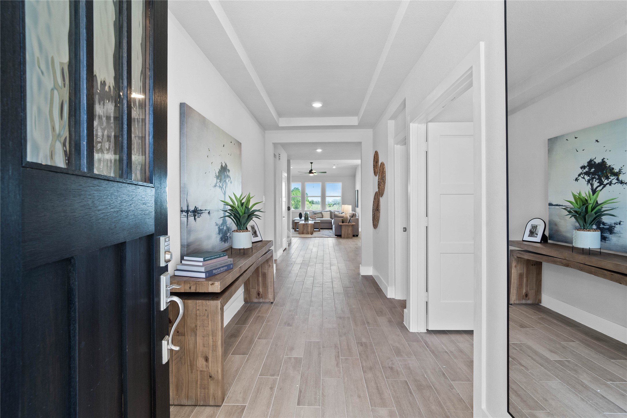 This entryway features a modern, open-concept design. The long, wide, and bright corridor utilizes a neutral color palette, recessed lighting, and wood-look tile flooring to lead the eye toward the home's main living area.