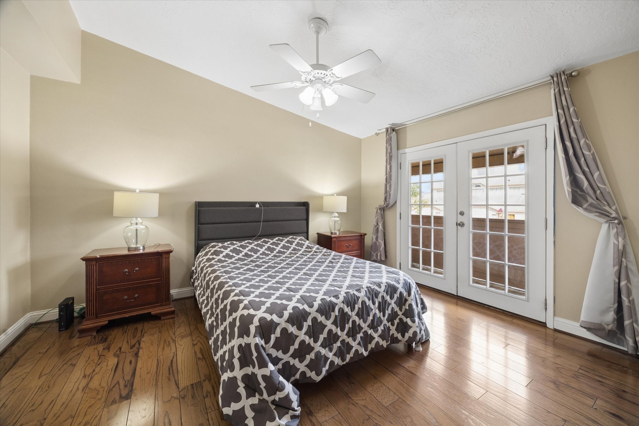 Spacious primary bedroom with hardwood floors, neutral finishes, ceiling fan, and French doors that bring in natural light and add architectural charm. Spacious primary bedroom with hardwood floors, neutral finishes, ceiling fan, and French doors that bring in natural light and add architectural charm.
